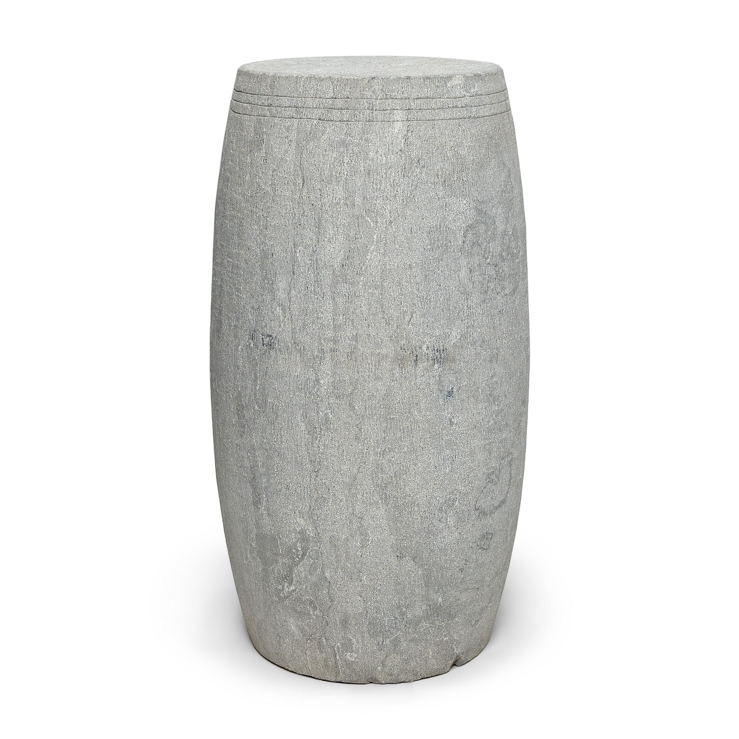 This narrow drum stool was carved from a solid block of limestone with a minimalist tapered design. The stool is subtly etched with thin grooves around the top, suggestive of the lines drawn by stretched hide on an actual drum. Traditionally used as