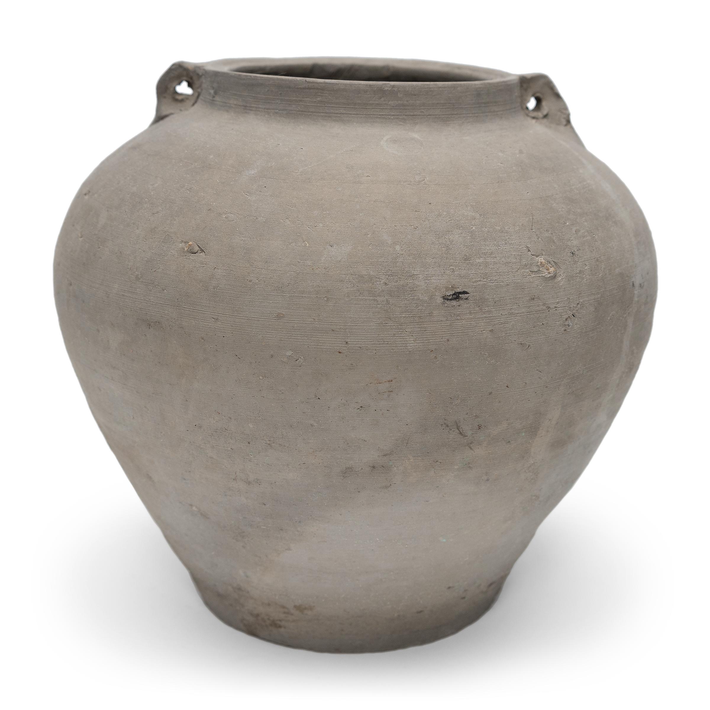 Charged with the humble task of storing dry goods, this small earthenware jar was hand-shaped in the early 20th century with balanced proportions and a beautifully irregular unglazed surface. The round jar has a tapered form with a narrow base, high