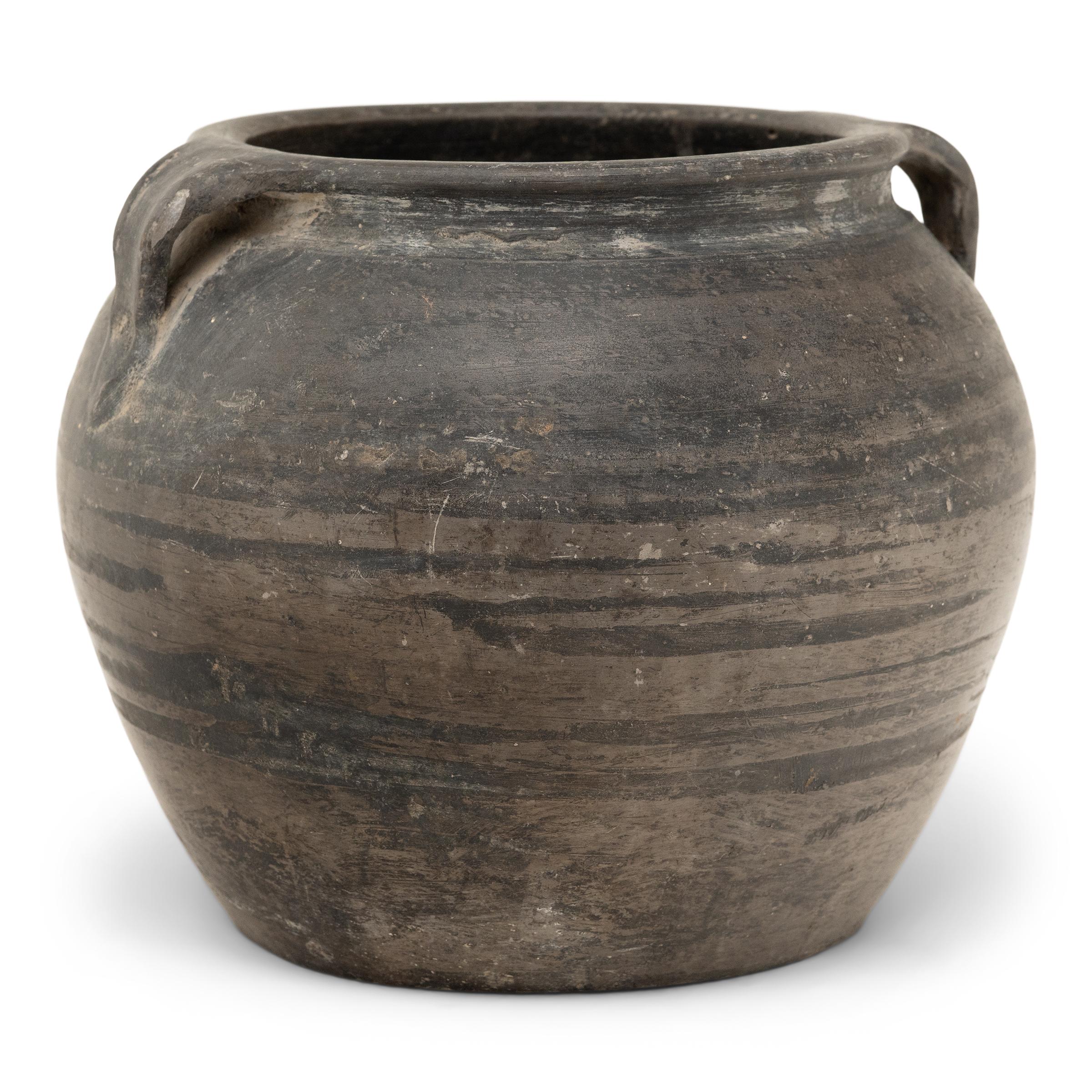 Con l'umile compito di conservare le merci secche, questo piccolo vaso di terracotta è stato modellato a mano all'inizio del XX secolo con proporzioni equilibrate e una superficie non smaltata splendidamente irregolare. Il vaso rotondo ha una forma