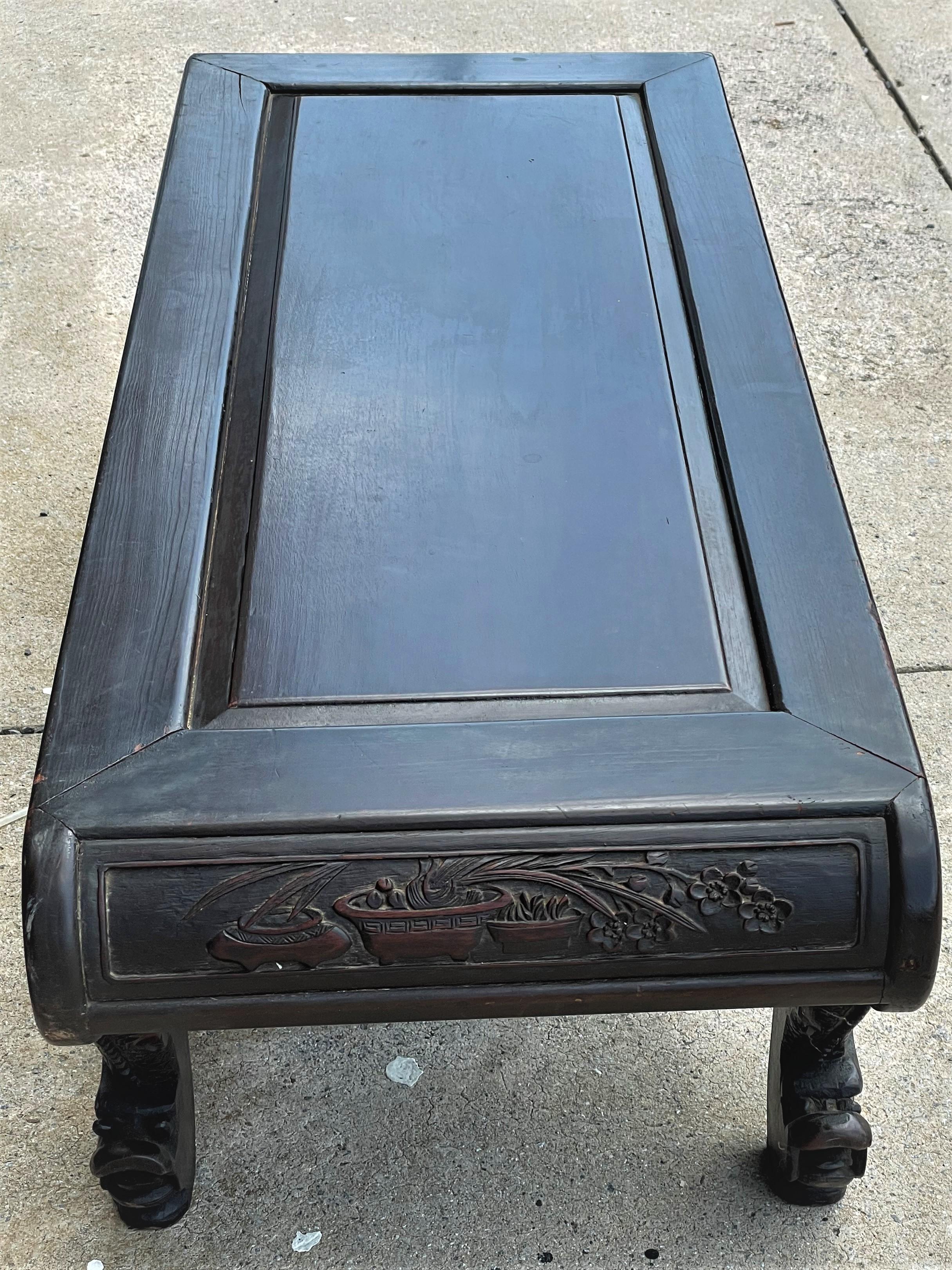 This is a wonderful, finely carved Kang low table or bench, which originally would have even been used as a bed. It has exotic dragon carved legs with the dragon head being the feet. The scrolled ends are carved in relief on the outside but have