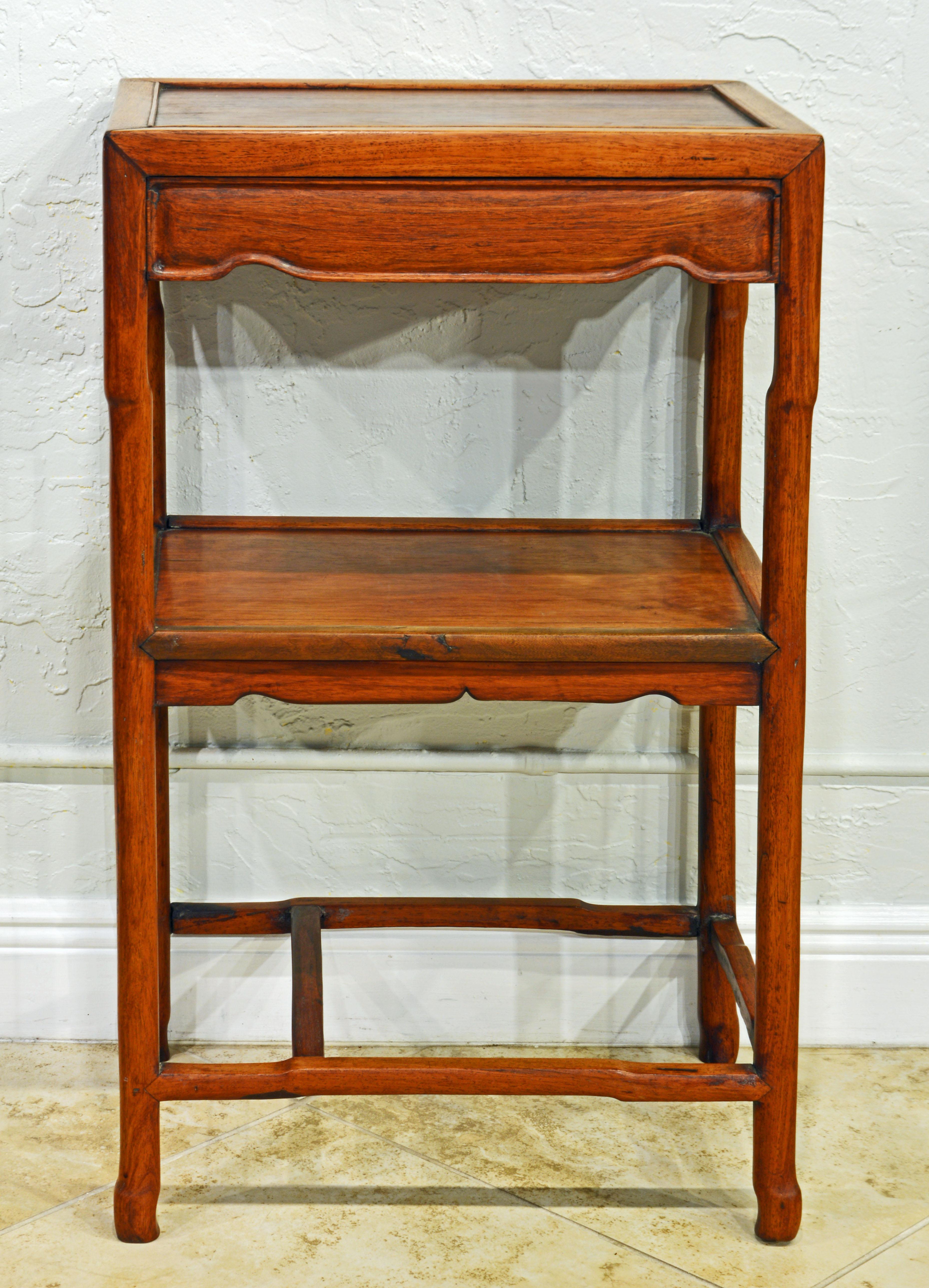 This refined Chinese two tier Huanghuali stand represents the refined design of the Ming period and is likely made in the mid 19th century or earlier. It features a paneled top above carved apron panels and four delicately shaped legs ending in