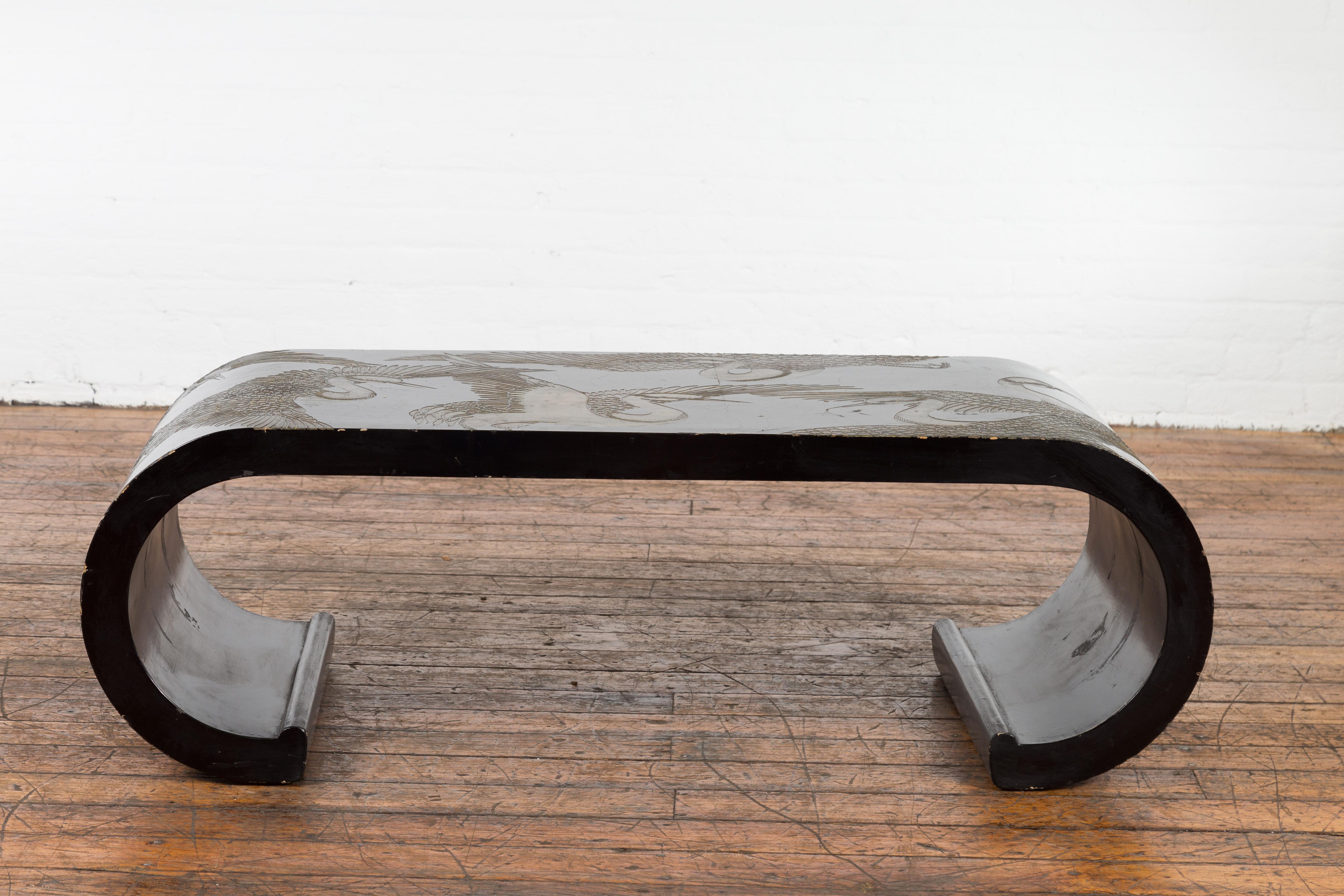 A Chinese vintage waterfall scroll coffee table from the Mid-20th Century, with black lacquer and reserved décor depicting elegant birds. Created in China during the Midcentury period, this vintage waterfall coffee table attracts our attention with