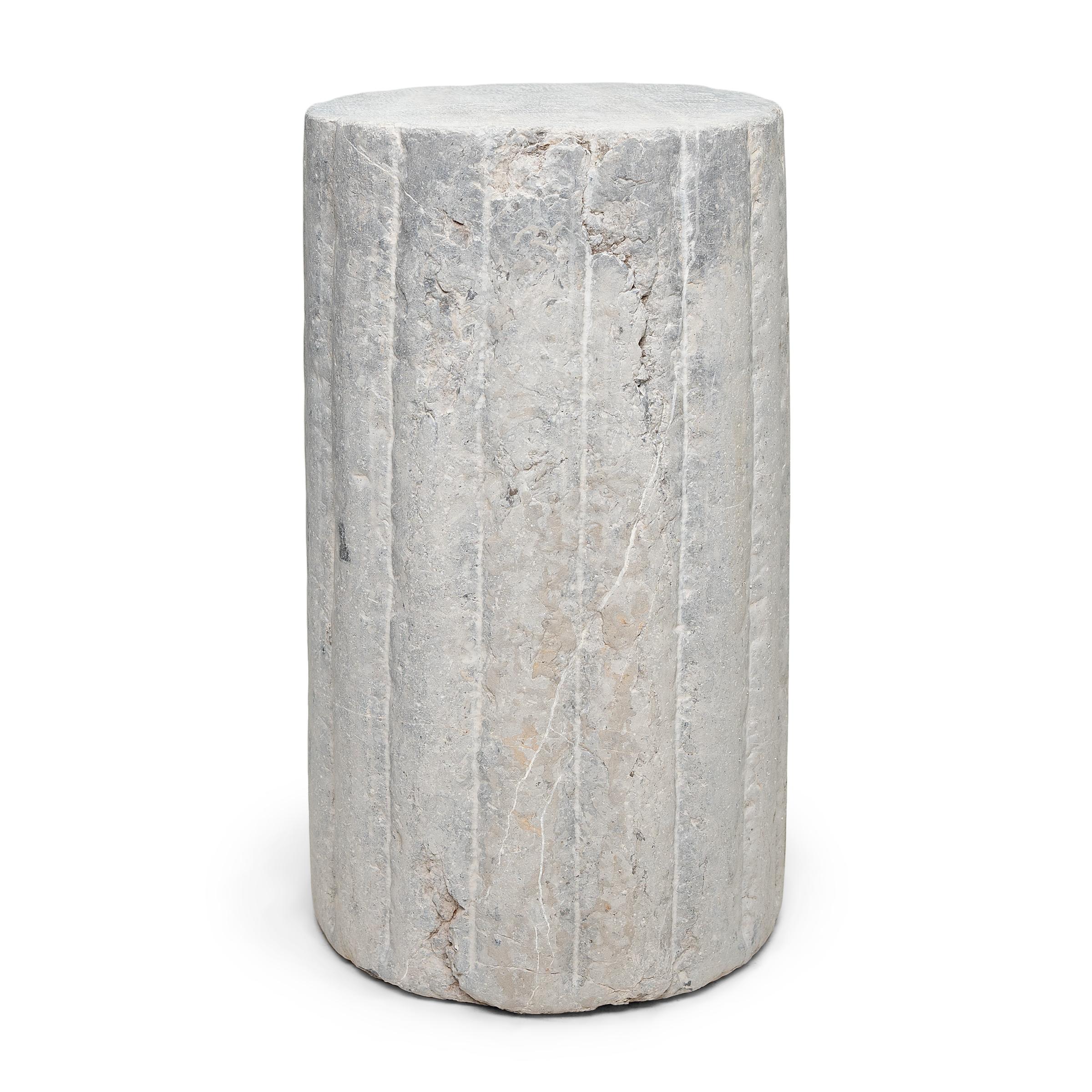 Ce piédestal en pierre inhabituel est en fait une pierre de moulin cylindrique datant de la fin du XIXe siècle. Sculptée à la main dans une pierre calcaire massive à la surface texturée et nervurée, cette pierre était utilisée pour battre le blé et