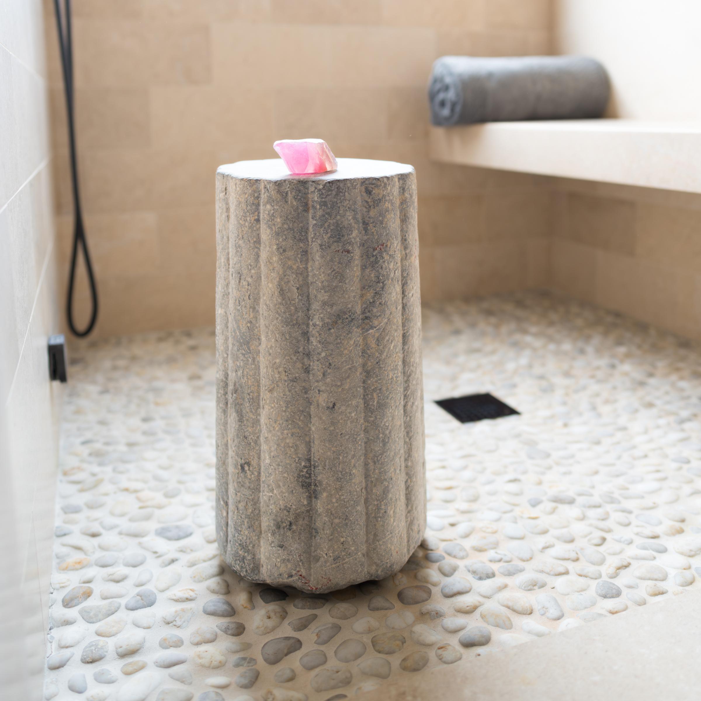 Ce piédestal en pierre inhabituel est en fait une pierre de moulin cylindrique datant de la fin du XIXe siècle. Sculptée à la main dans une pierre calcaire massive à la surface texturée et nervurée, cette pierre était utilisée pour battre le blé et