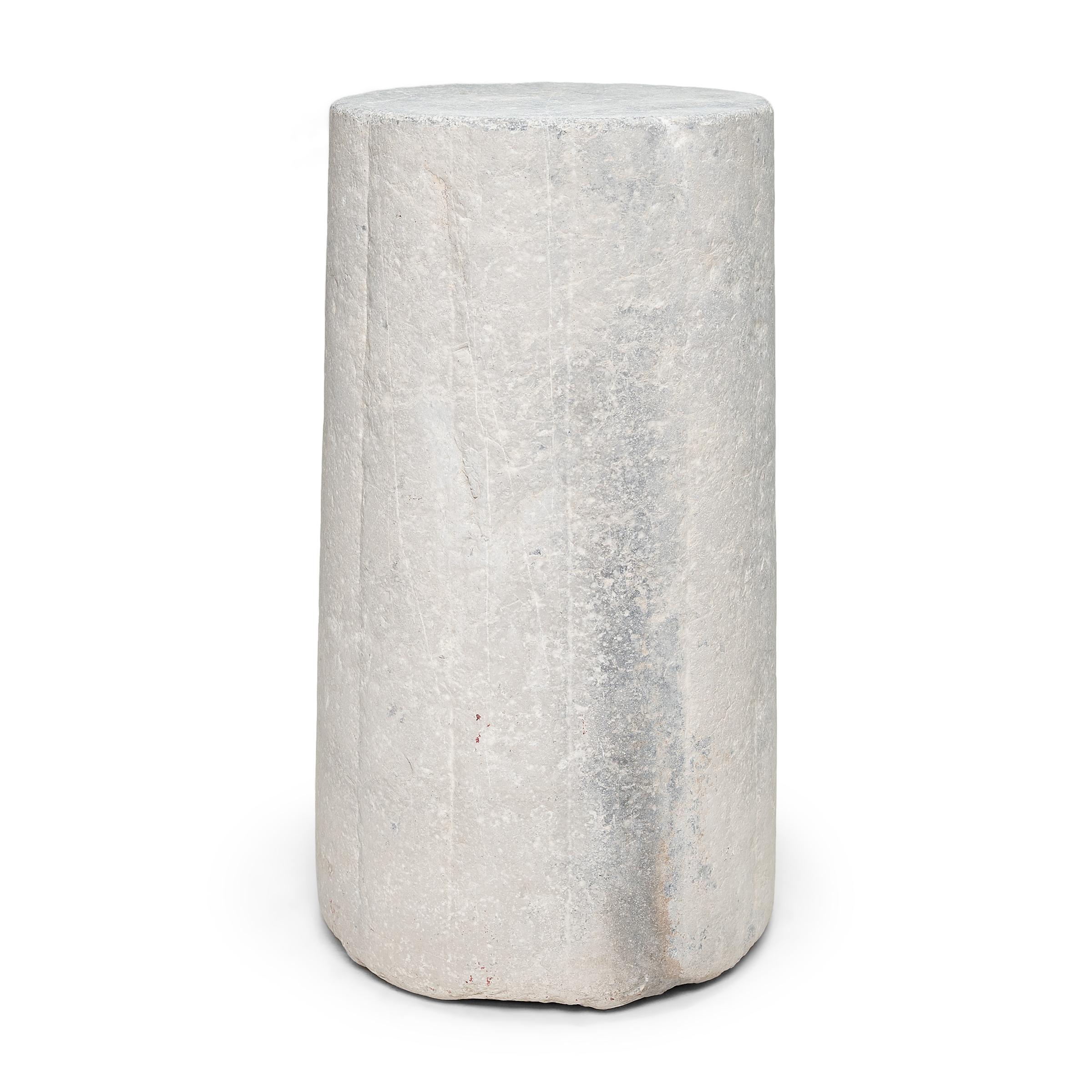 Ce piédestal en pierre inhabituel est en fait une pierre de moulin cylindrique datant de la fin du XIXe siècle. Sculptée à la main dans une pierre calcaire massive à la surface texturée et nervurée, cette pierre était utilisée pour battre le blé et