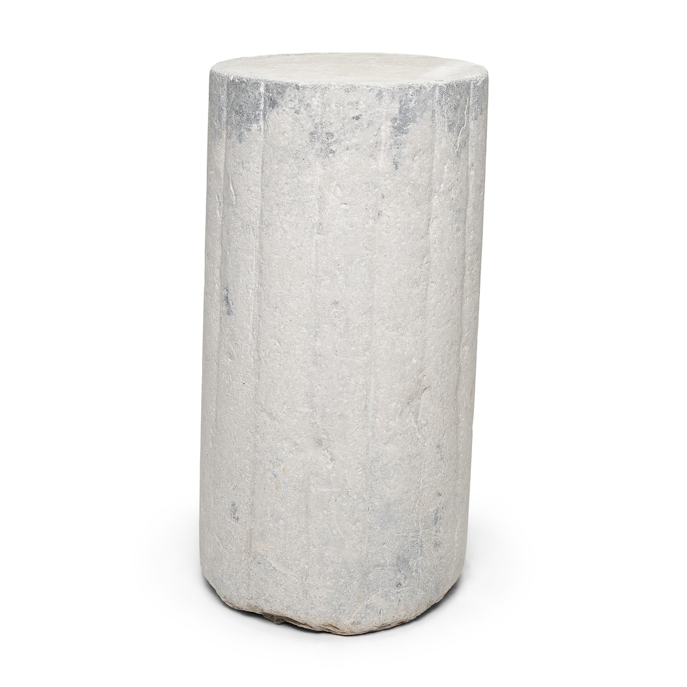 This unusual stone pedestal is actually a late 19th century cylindrical mill stone. hand carved of solid limestone with a textured and ribbed surface, the stone was used for threshing wheat and other grains on a farm in China's Shanxi province. The