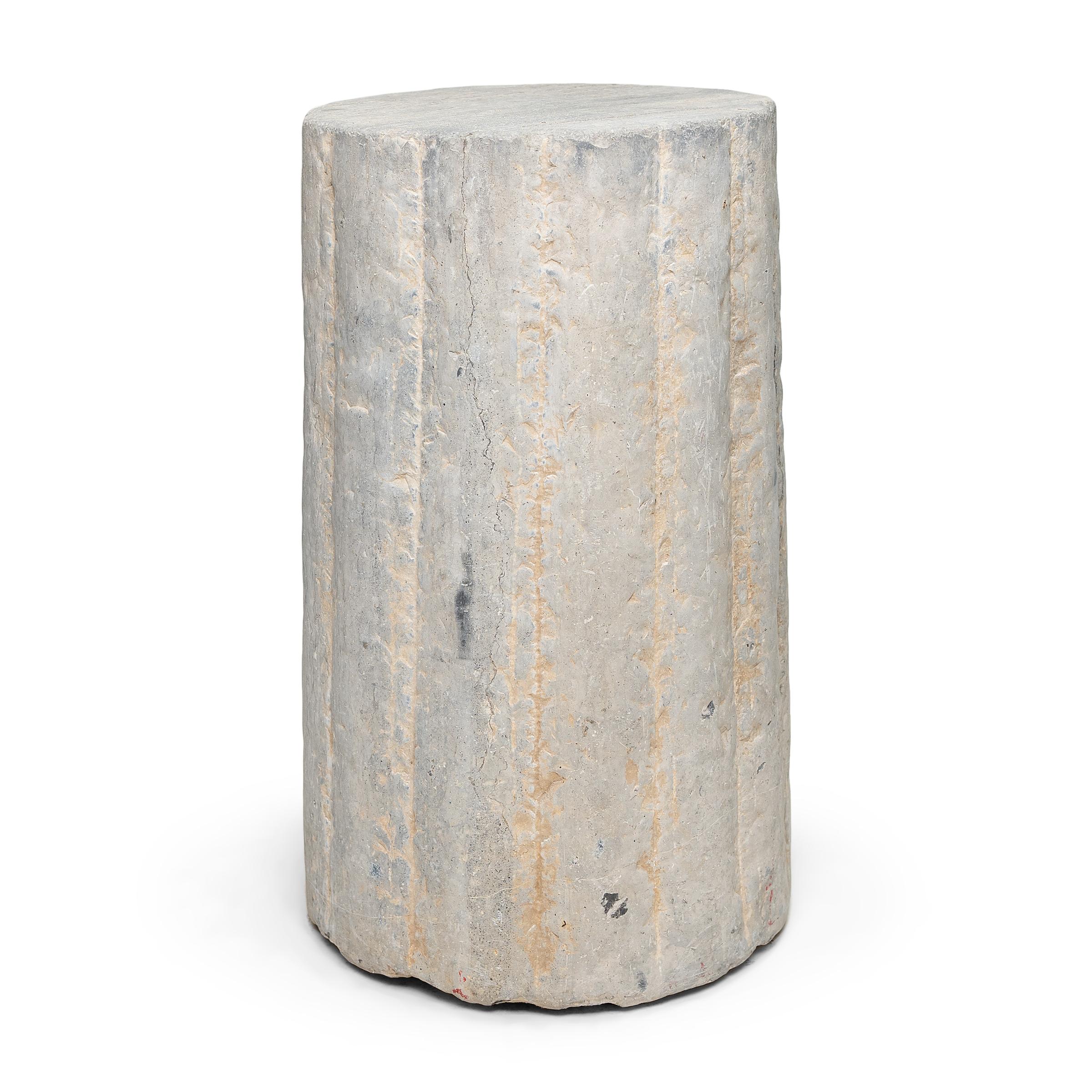 This unusual stone pedestal is actually a late 19th century cylindrical mill stone. hand carved of solid limestone with a textured and ribbed surface, the stone was used for threshing wheat and other grains on a farm in China's Shanxi province. The