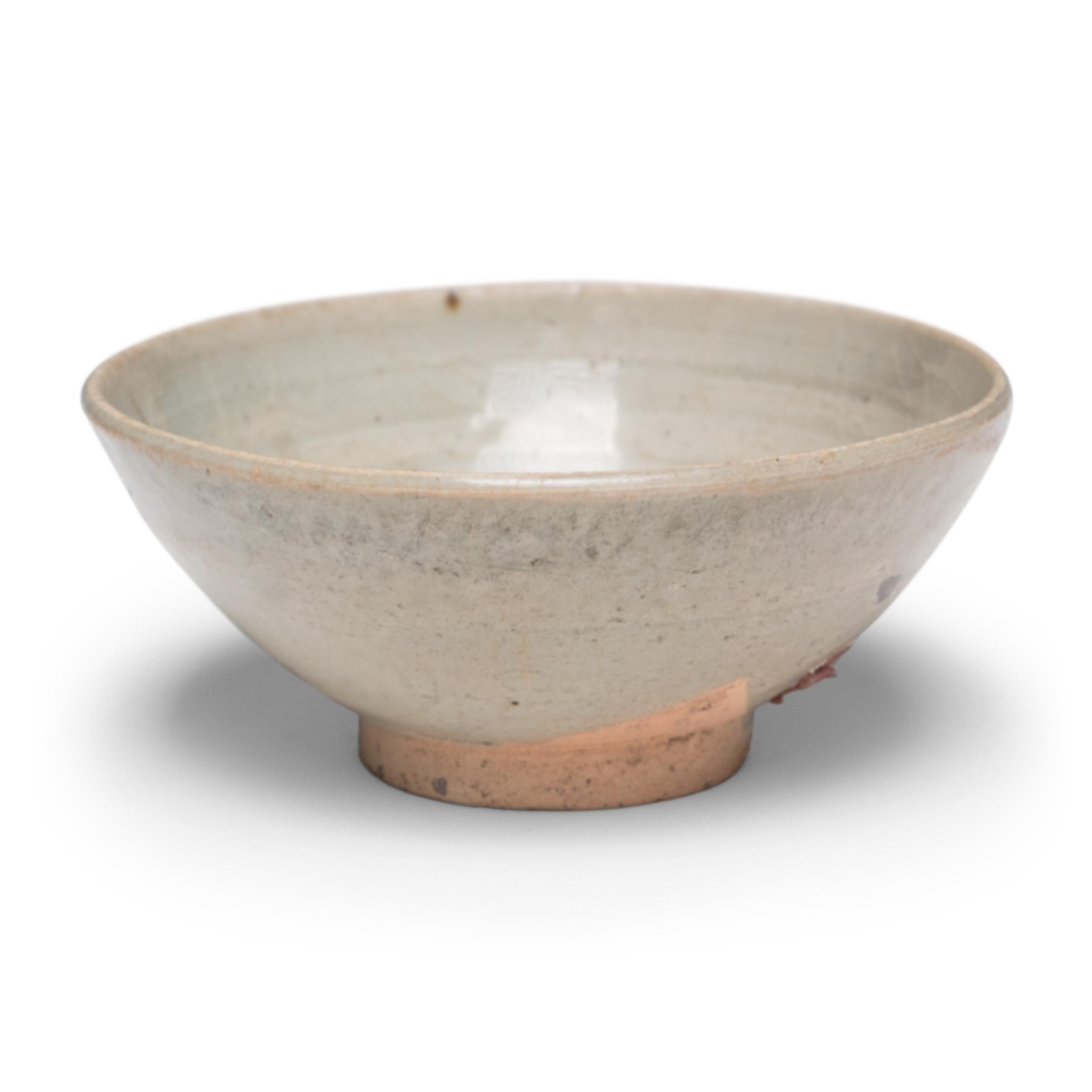 Ce bol en faïence de la fin de la dynastie Ming (1368-1644) est recouvert à l'intérieur et à l'extérieur d'une glaçure céladon cendrée de couleur gris pâle et de fines craquelures. Autrefois utilisé quotidiennement pour boire et manger, le bol est