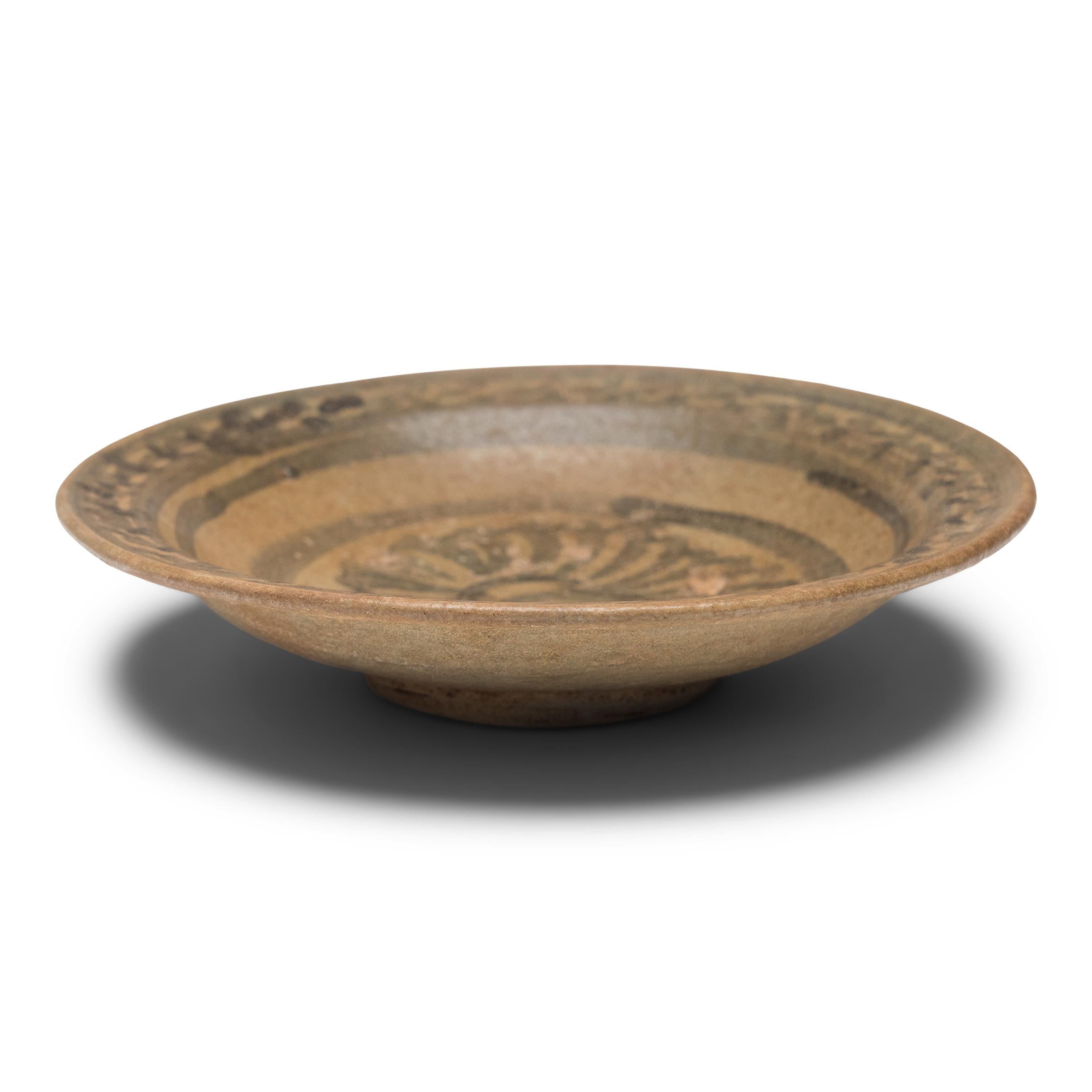 This Ming-dynasty (1368-1644) plate is attributed to the kilns of Yunnan province, painted in cobalt underglaze with a chrysanthemum blossom and sweeping brushstrokes. Dated to the 15th/16th century, the earthenware dish is potted with thick walls