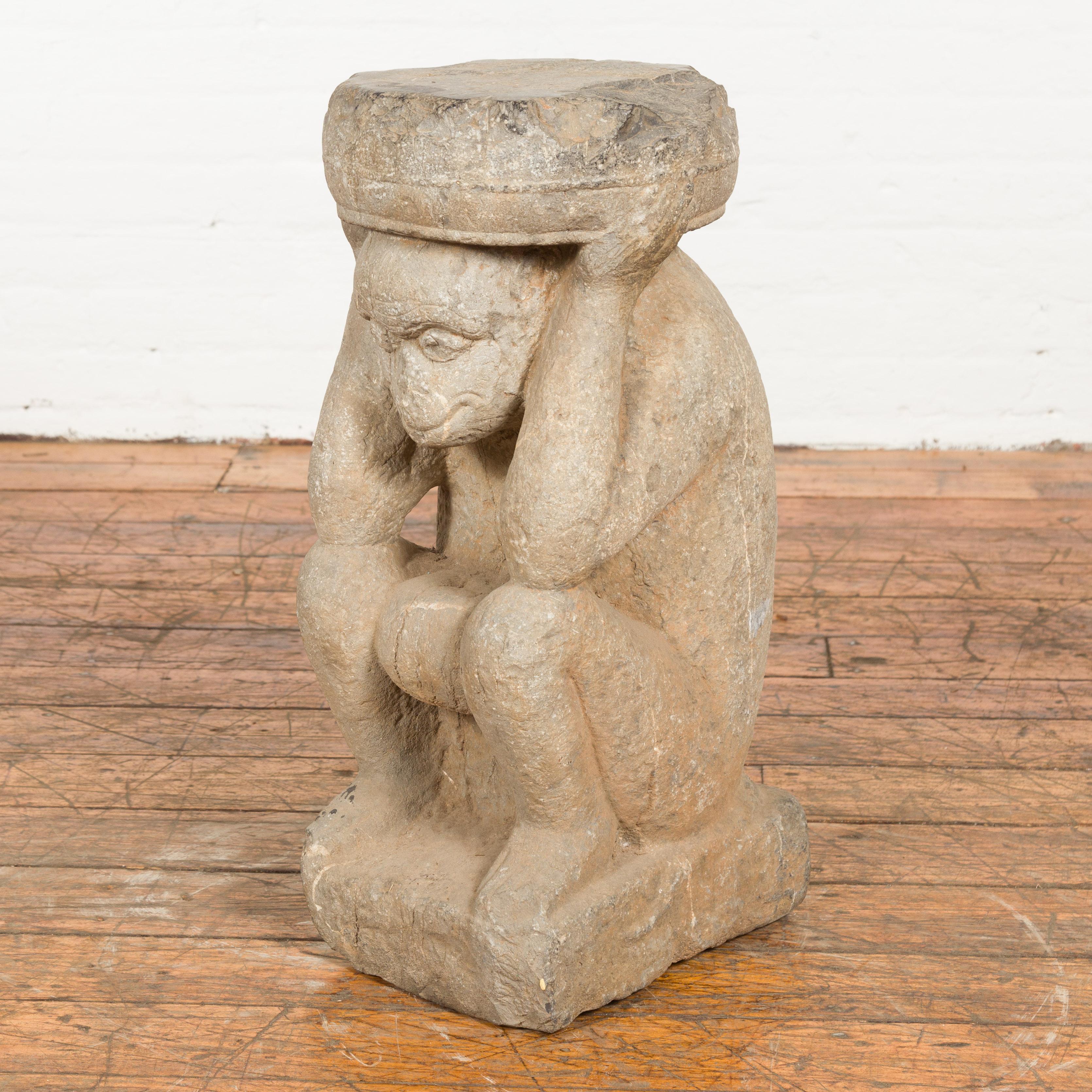 A Chinese Ming Dynasty period hand carved stone monkey temple sculpture from the 17th century, depicted seated and holding a round stone disc above its head. Created in China during the Ming Dynasty period which spanned from 1368 to 1644, this hand