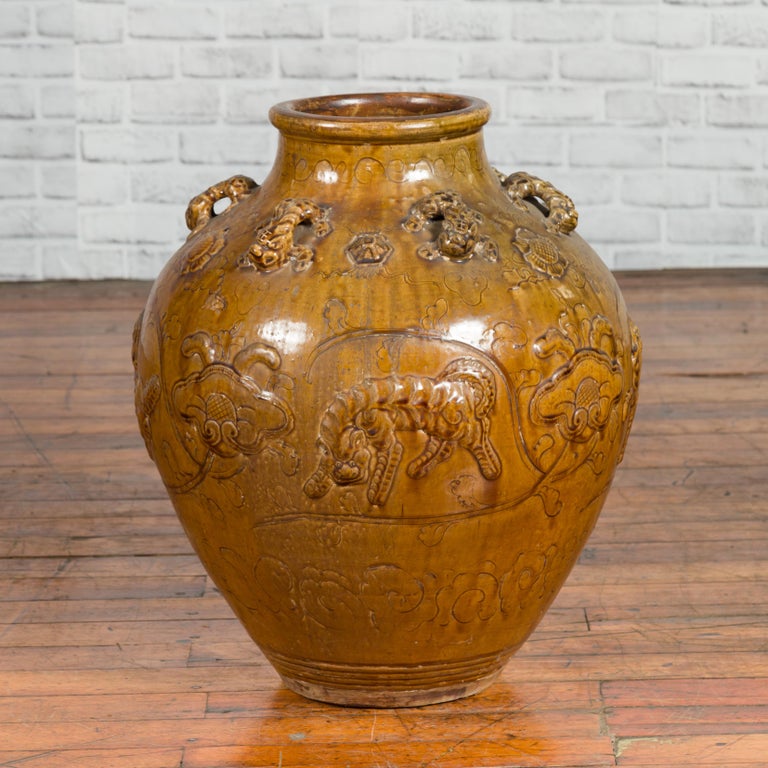 A Chinese Ming Dynasty period glazed ceramic Martaban water jar from the 17th century, with tiger motifs and petite handles. Created in China during the Ming Dynasty era, this Martaban water jar features a golden brown patina perfectly accented with