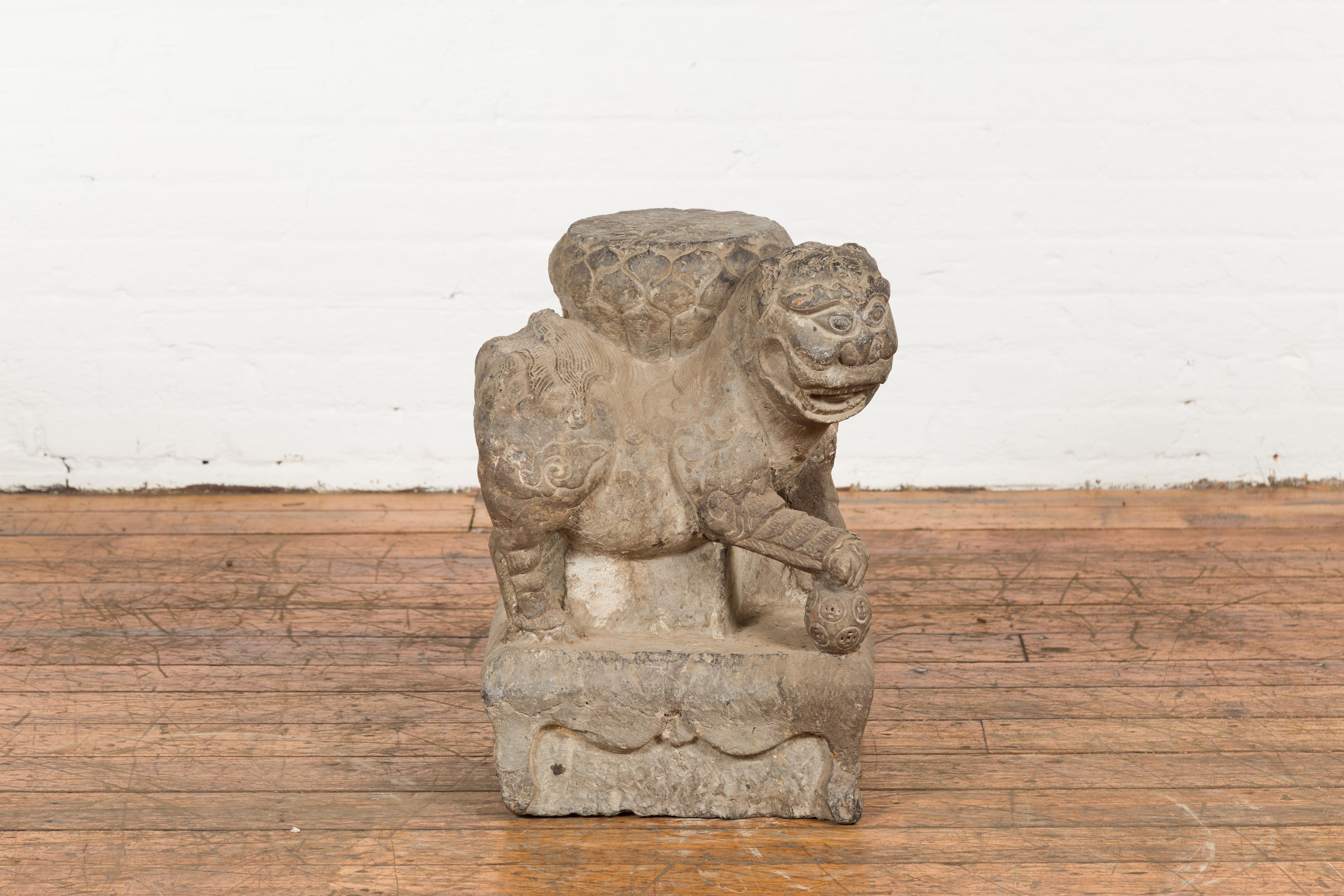 A Chinese Ming Dynasty period (1368 - 1644) hand-carved stone Foo Dog guardian lion sculpture depicting a male placing his paw atop a ball. Created in China during the Ming Dynasty which spanned from 1368 to 1644, this hand-carved stone sculpture