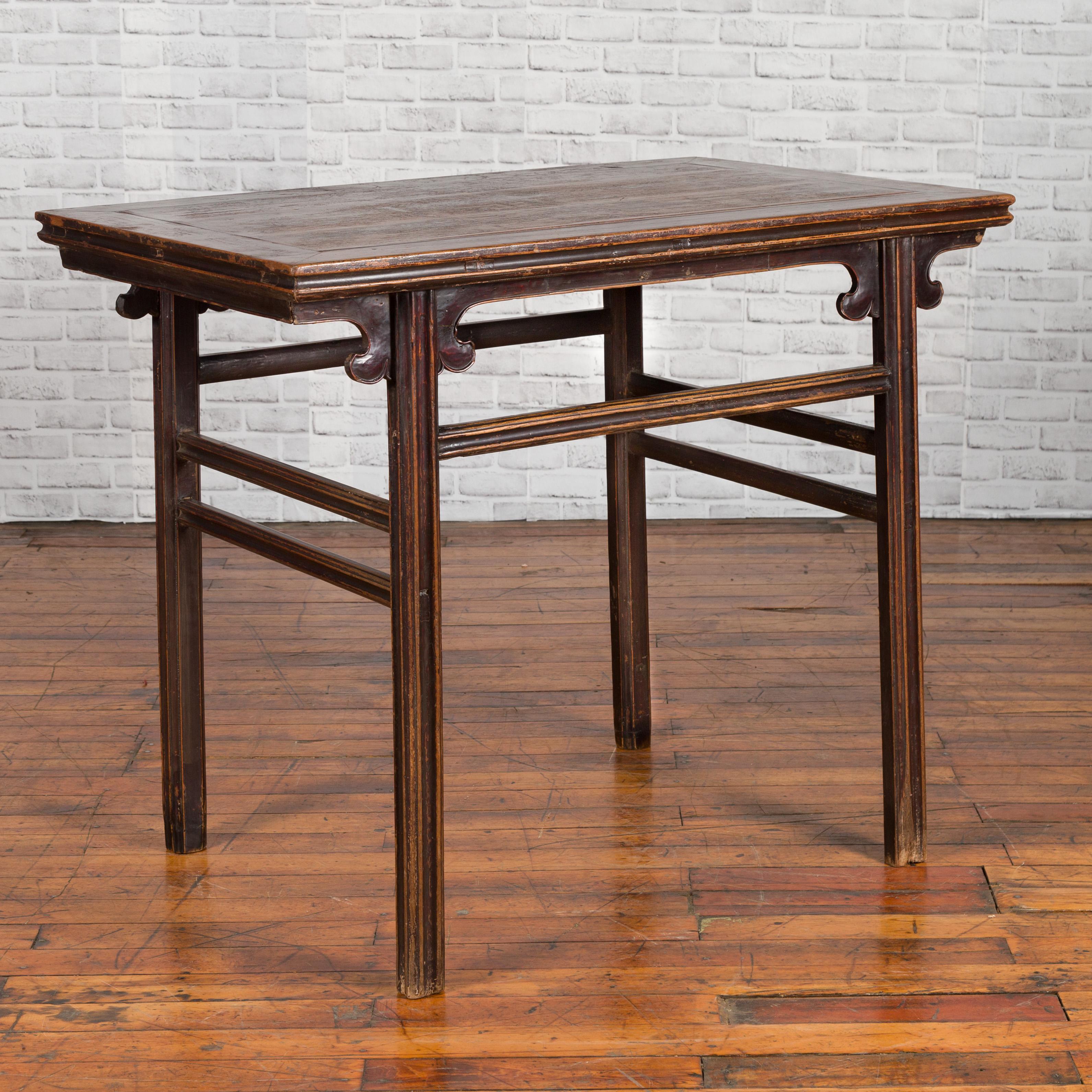 A Chinese Ming Dynasty style wine table from the 19th century, with carved spandrels and straight legs. Created in China during the Qing Dynasty, this antique wine table table features a rectangular top with central board, sitting above four