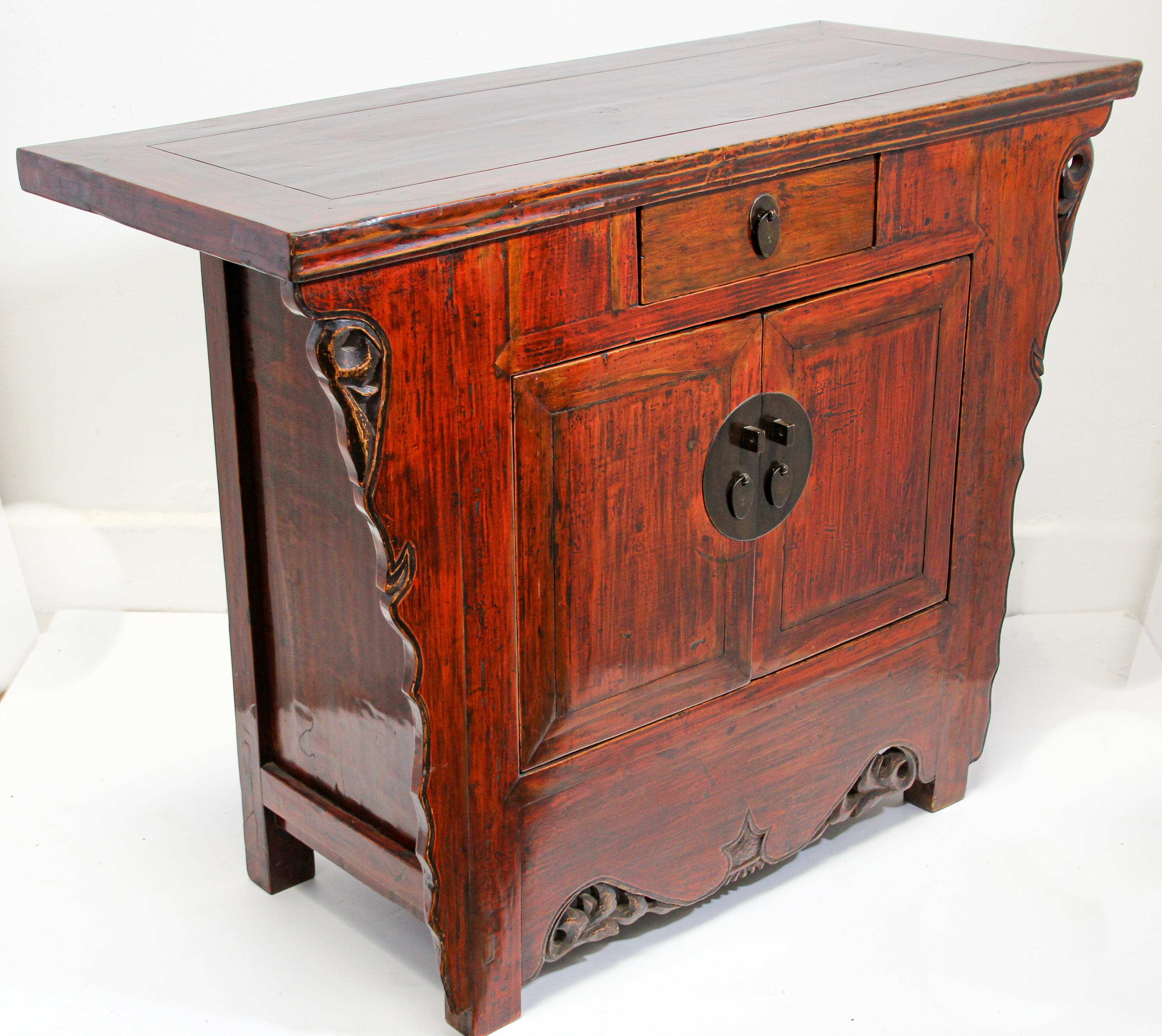 Chinese Ming style hand painted red and brown lacquered cabinet with carved sides, drawer and doors.
The piece features intricate hand carved details and an antique look patina. 
Behind its two doors is ample storage, including a single