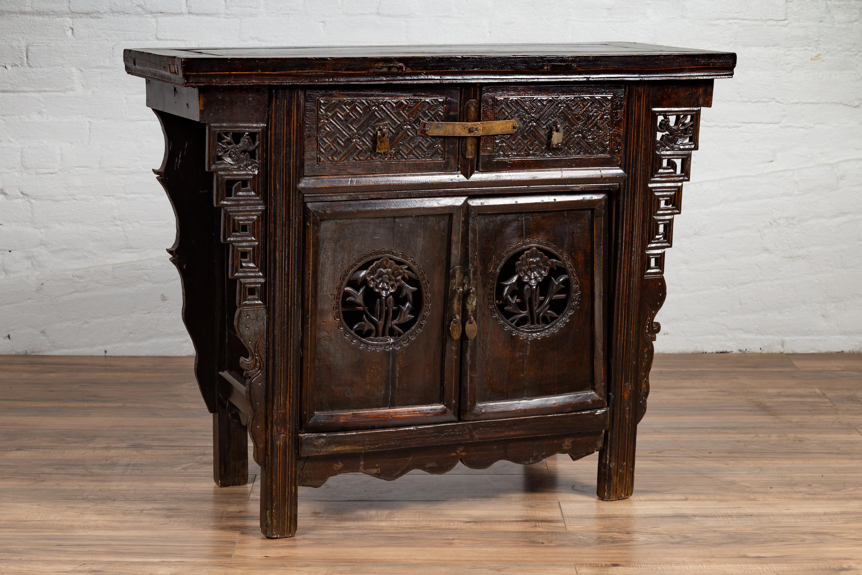 A Chinese Ming Dynasty style wooden butterfly cabinet from the 19th century, with carved spandrels, drawers, doors and dark patina. Born in China during the 19th century, this exquisite coffer called a butterfly cabinet, features a rectangular