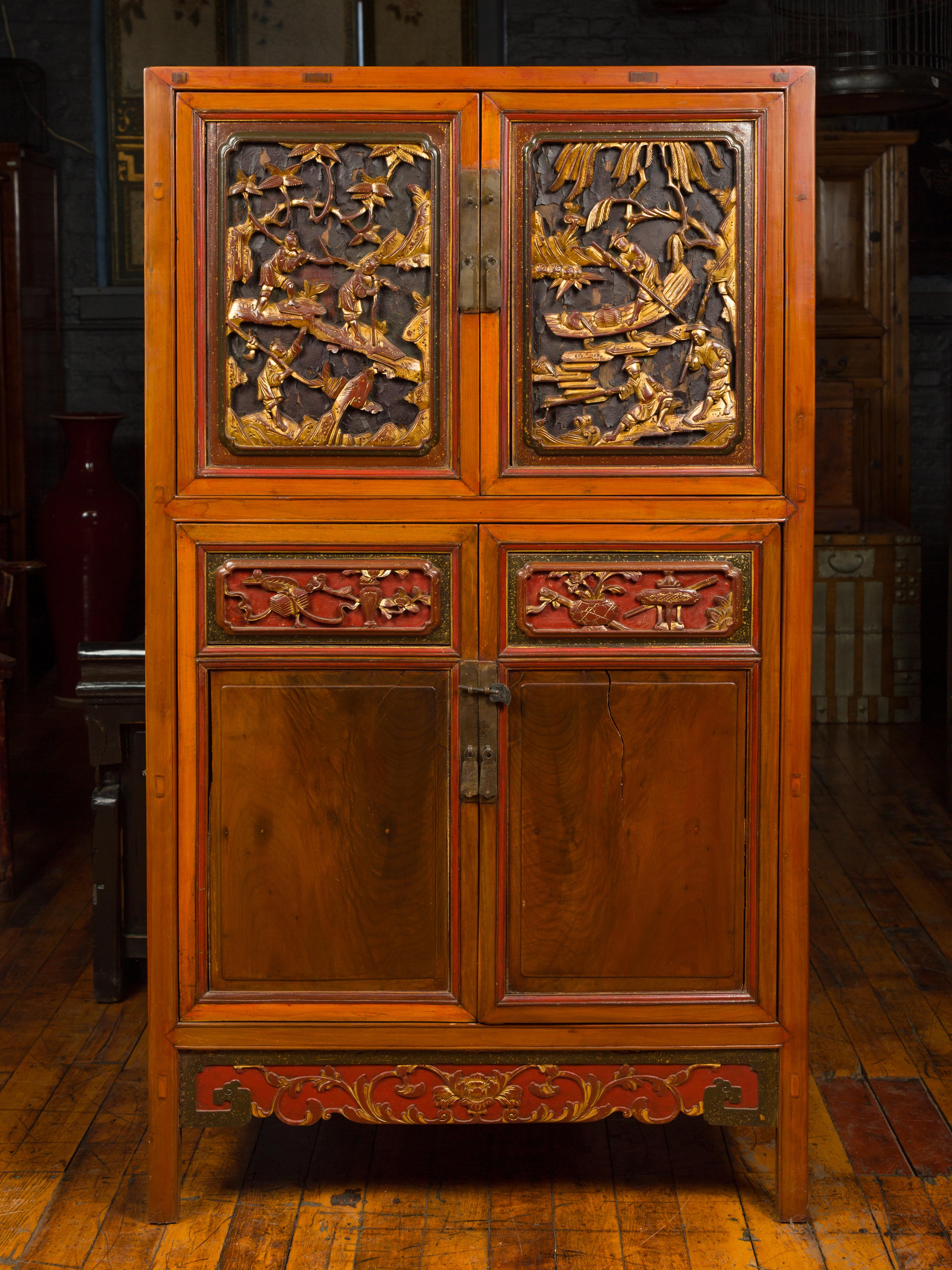 An antique Chinese Ming dynasty style cabinet from the 19th century, with four doors, two drawers, carved giltwood motifs and red accents. Born in China during the 19th century, this wooden cabinet captures our attention with its contrast of colors