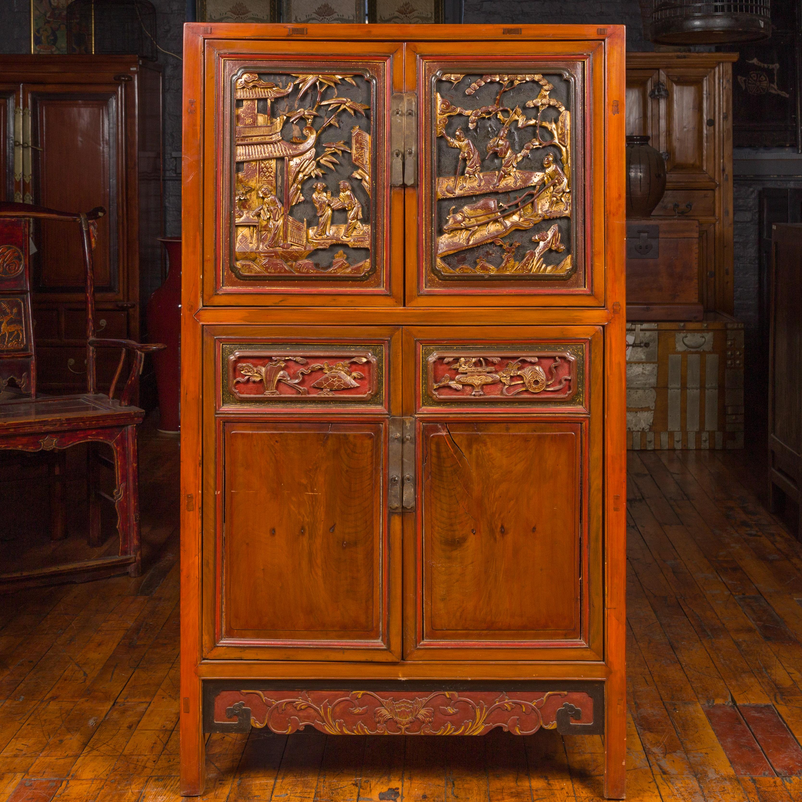 An antique Chinese Ming dynasty style cabinet from the 19th century, with two pairs of double doors, two drawers, carved giltwood motifs and red accents. Born in China during the 19th century, this wooden cabinet captures our attention with its