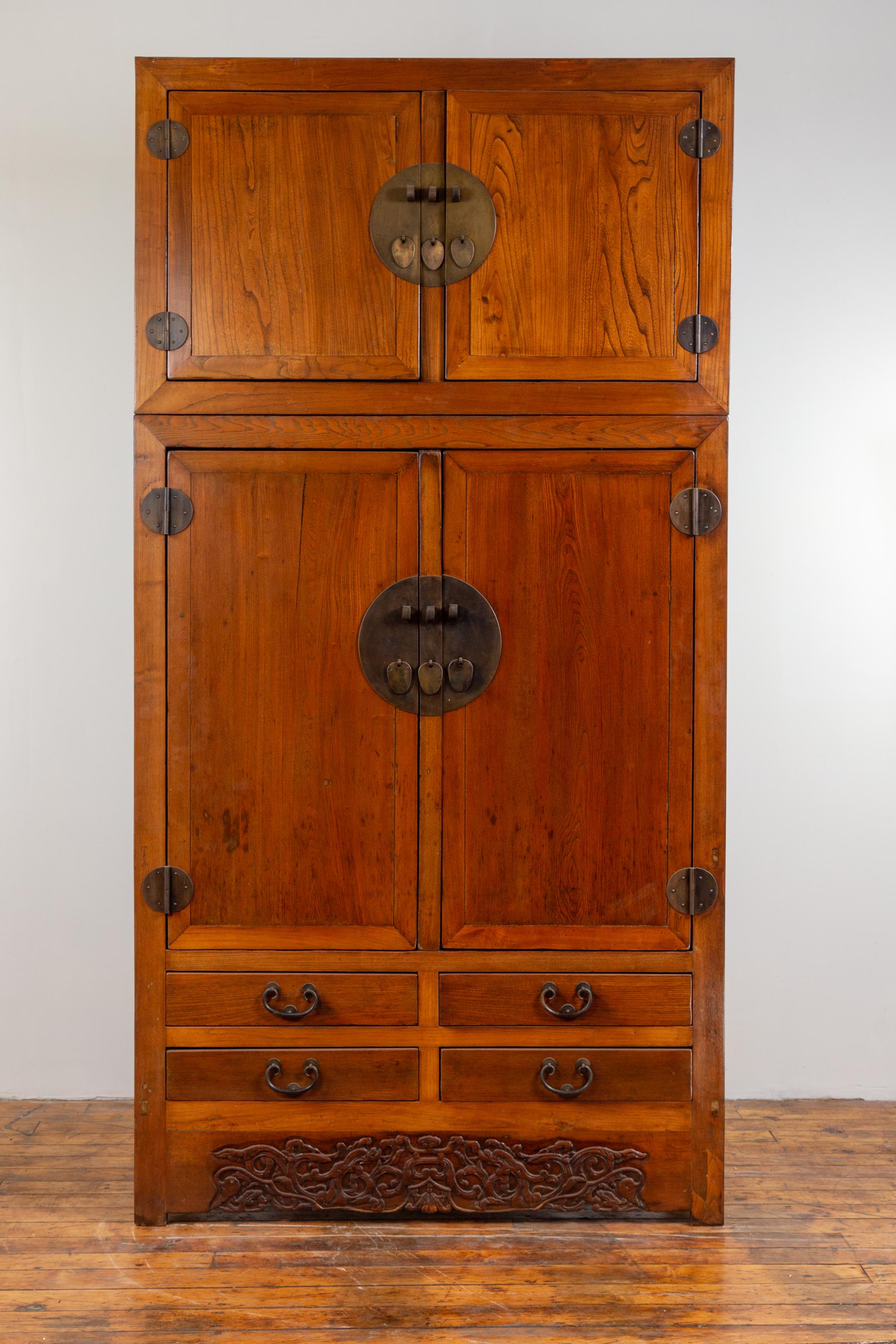 A Chinese Ming dynasty style two-section compound wedding wardrobe, with carved floral skirt, two sets of double doors, lower drawers and brass hardware. Born in China during the early years of the 20th century, this large compound wardrobe features