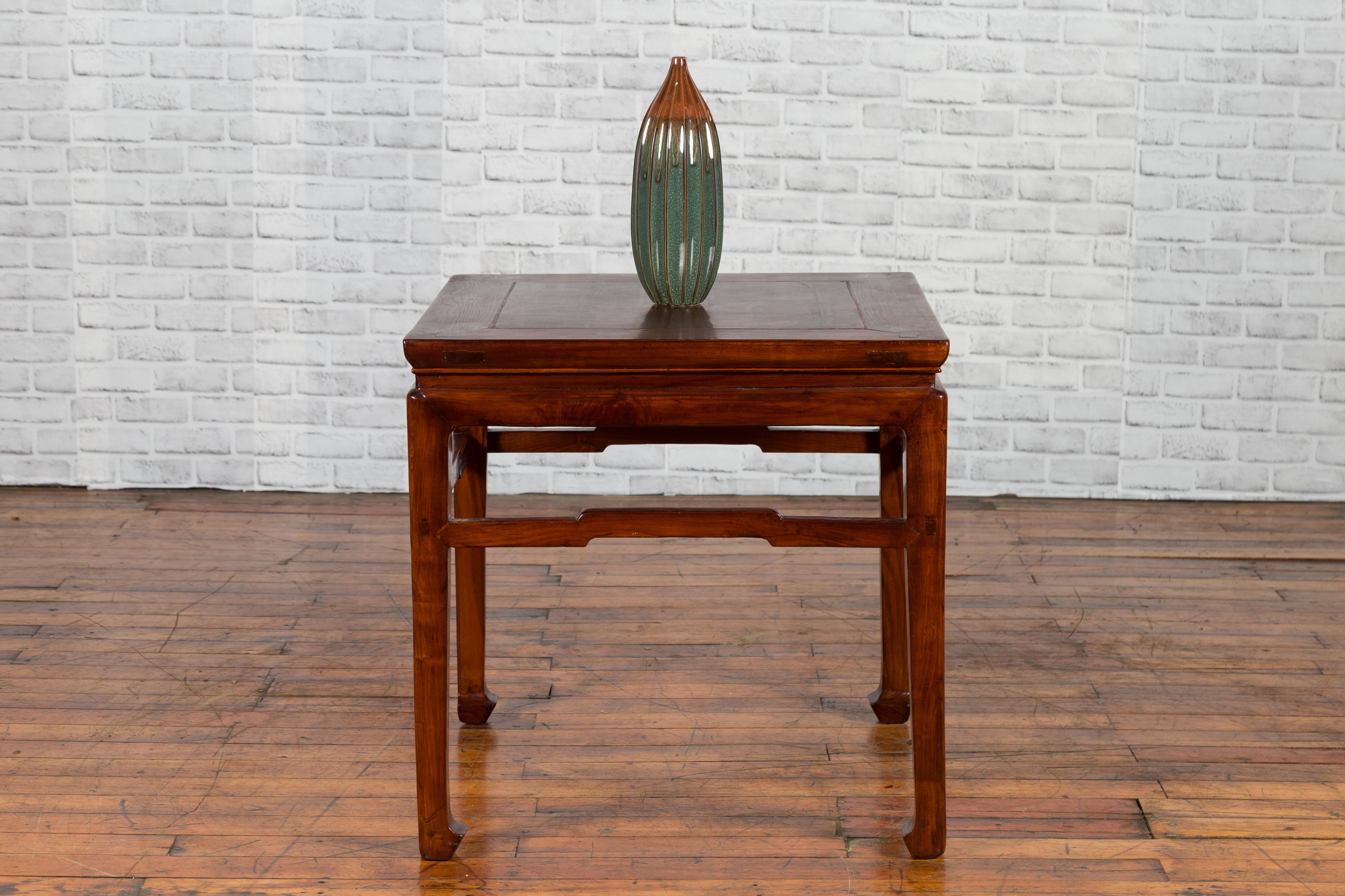 A Chinese Ming Dynasty style side table from the early 20th century, with humpbacked stretcher, horsehoof feet and waisted apron. Created in China during the early years of the 20th century, this side table, originally used as a stool, features a