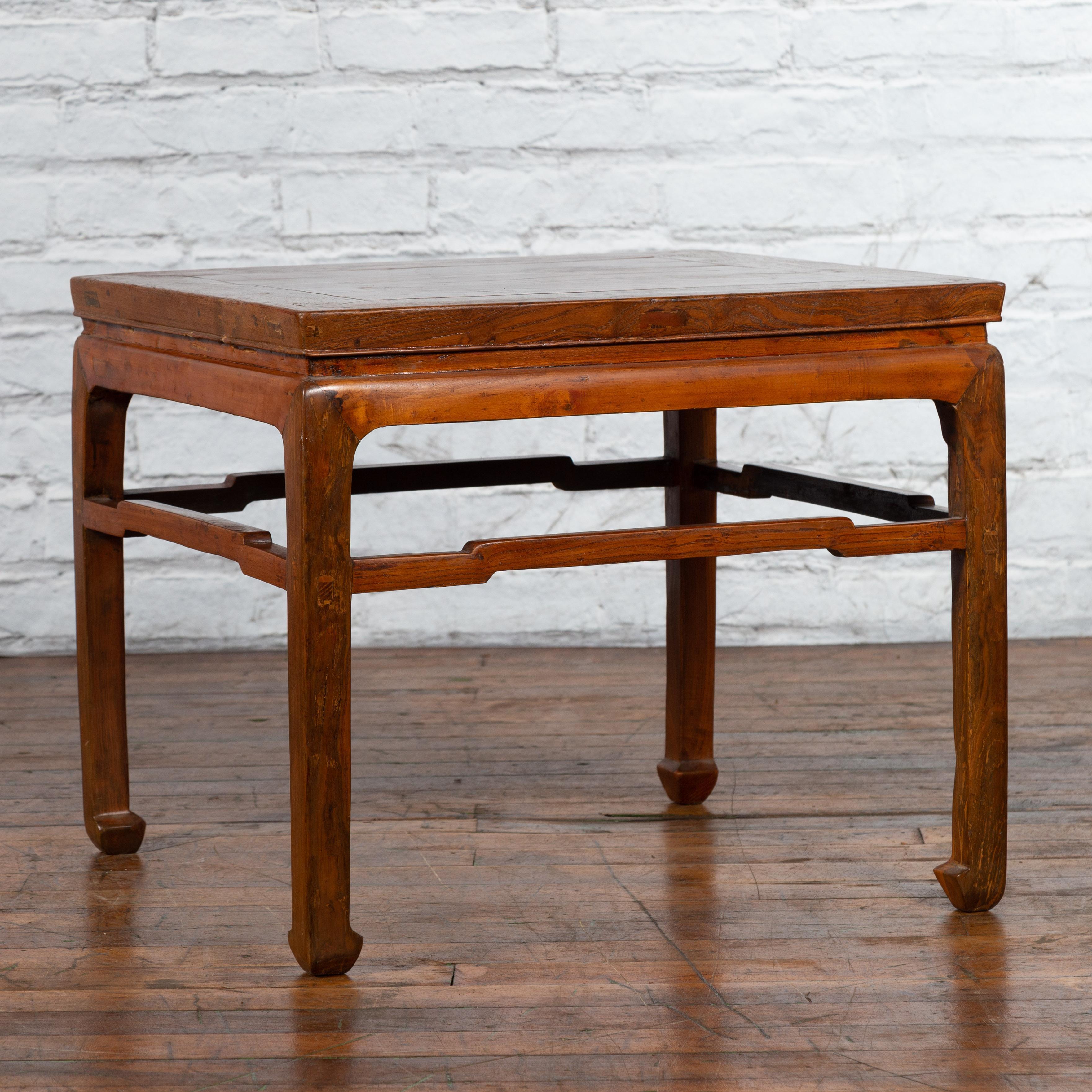 A Chinese Ming Dynasty style coffee table from the early 20th century, with humpbacked stretcher, horsehoof feet and waisted apron. Created in China during the early years of the 20th century, this coffee table features a square top with central