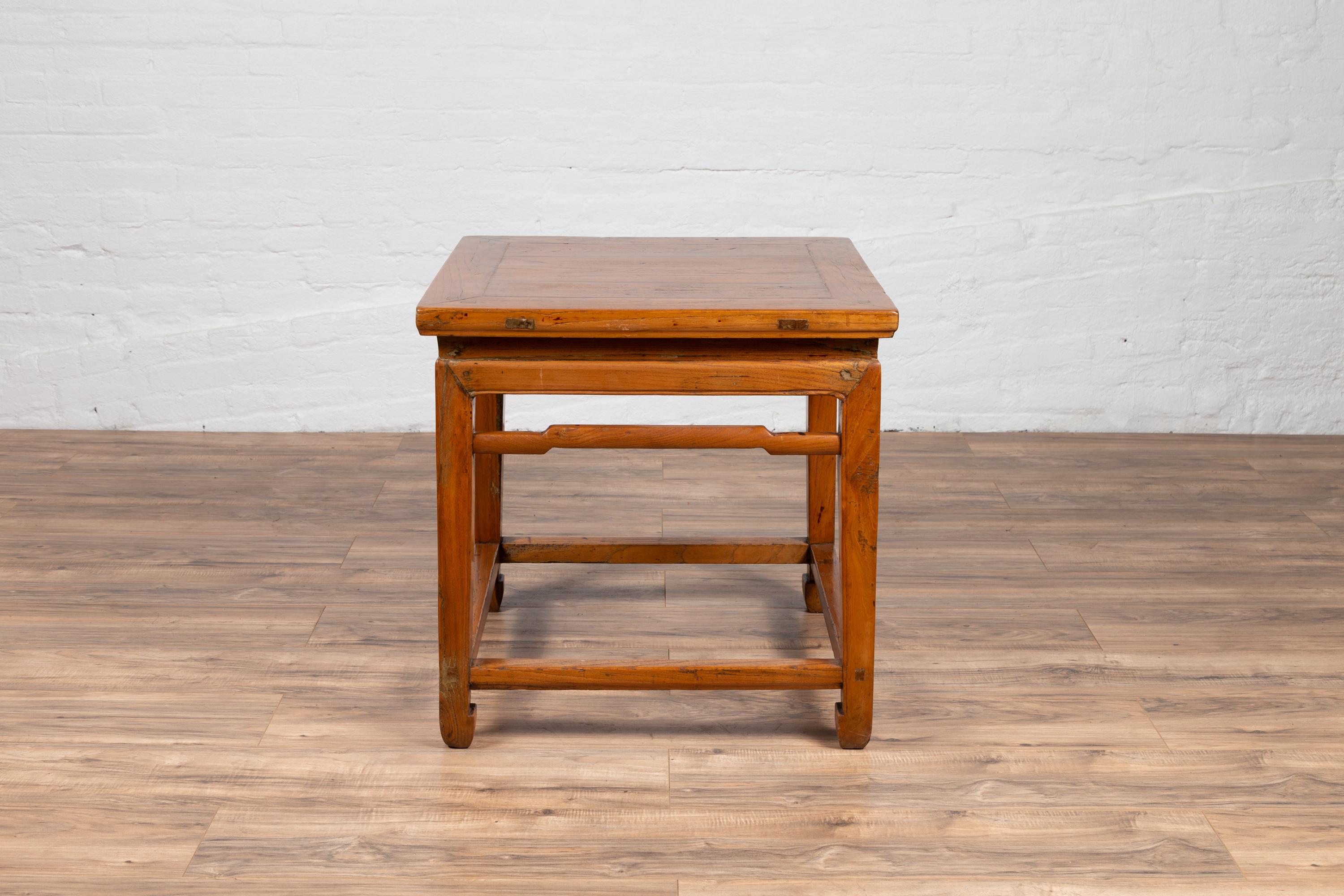 A Chinese Ming dynasty style waisted elmwood side table from the early 20th century, with humpbacked stretchers and horse-hoof feet. Born in China during the early years of the 20th century, this charming side table features a square top with