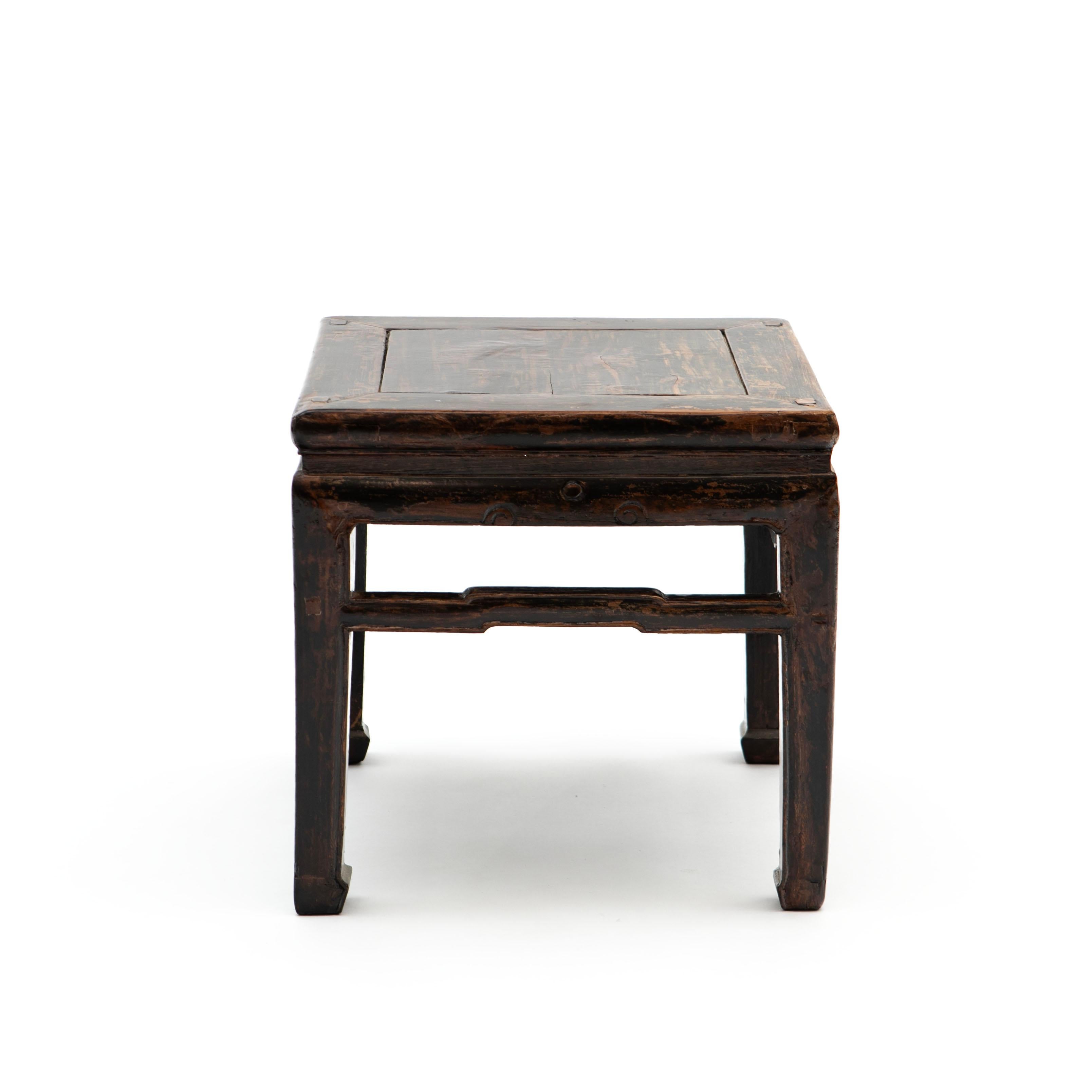 A Chinese antique ming style side lamp table from the late 19th century. Elm wood with original dark lacquer with natural age-related patina.
Features a square top with central board, sitting above a waisted apron raised on horse hoof feet and