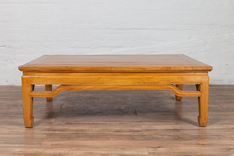 A Chinese Ming dynasty style natural wood coffee table with humpbacked apron and horse hoof legs. Born in China during the early years of the 20th century, this elegant coffee table features a natural wood finish complimenting beautifully the clean