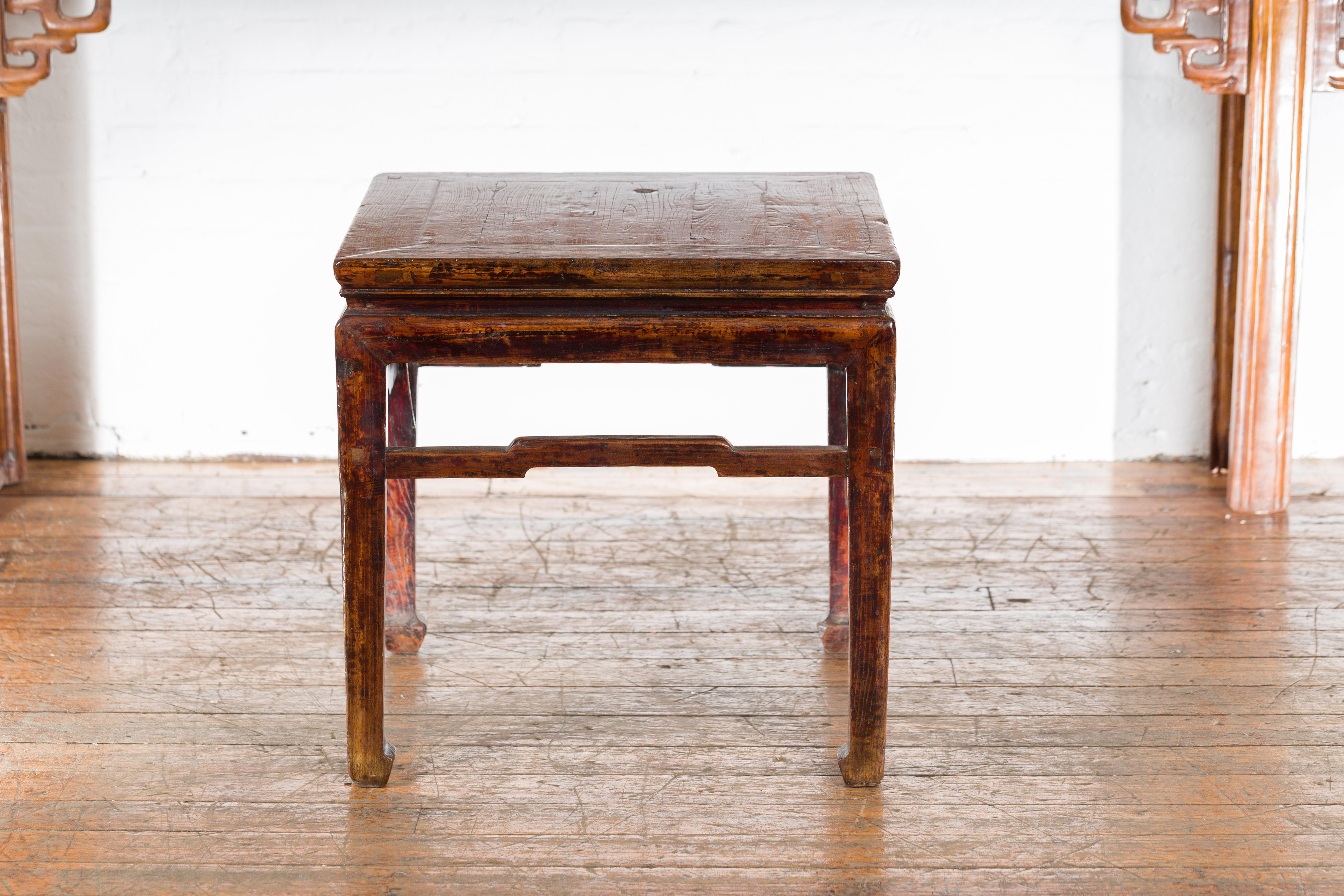 A Chinese vintage side lamp table from the mid 20th century, with horse hoof feet and humpback stretchers. Created in China during the midcentury period, this lamp table features a square top with central board, sitting above a waisted apron. The