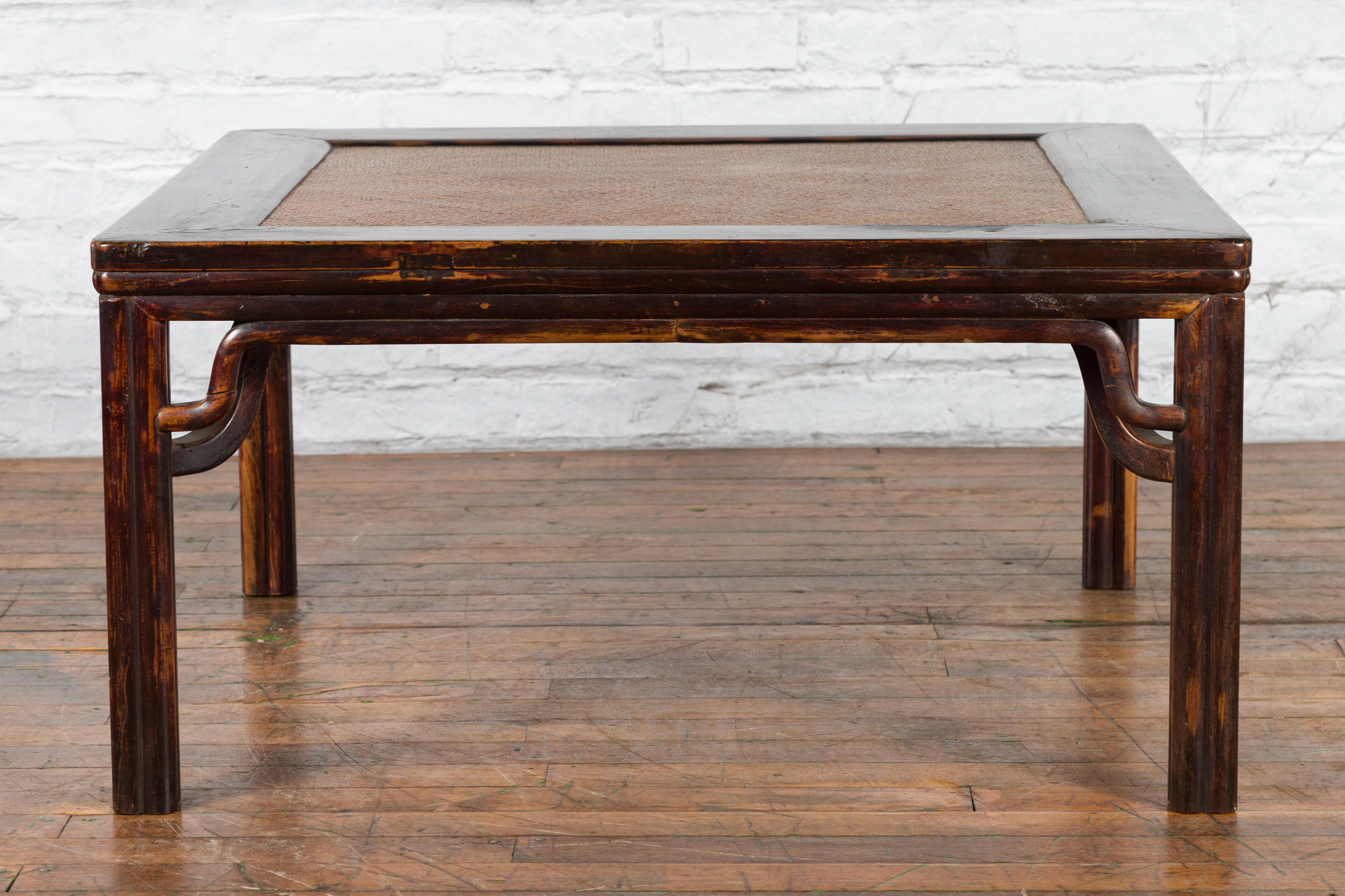 A Chinese Ming Dynasty style square-shaped wooden coffee table from the 19th century, with original distressed finish and hand-woven rattan top. Created in China during the Qing Dynasty period in the 19th century, this coffee table features the