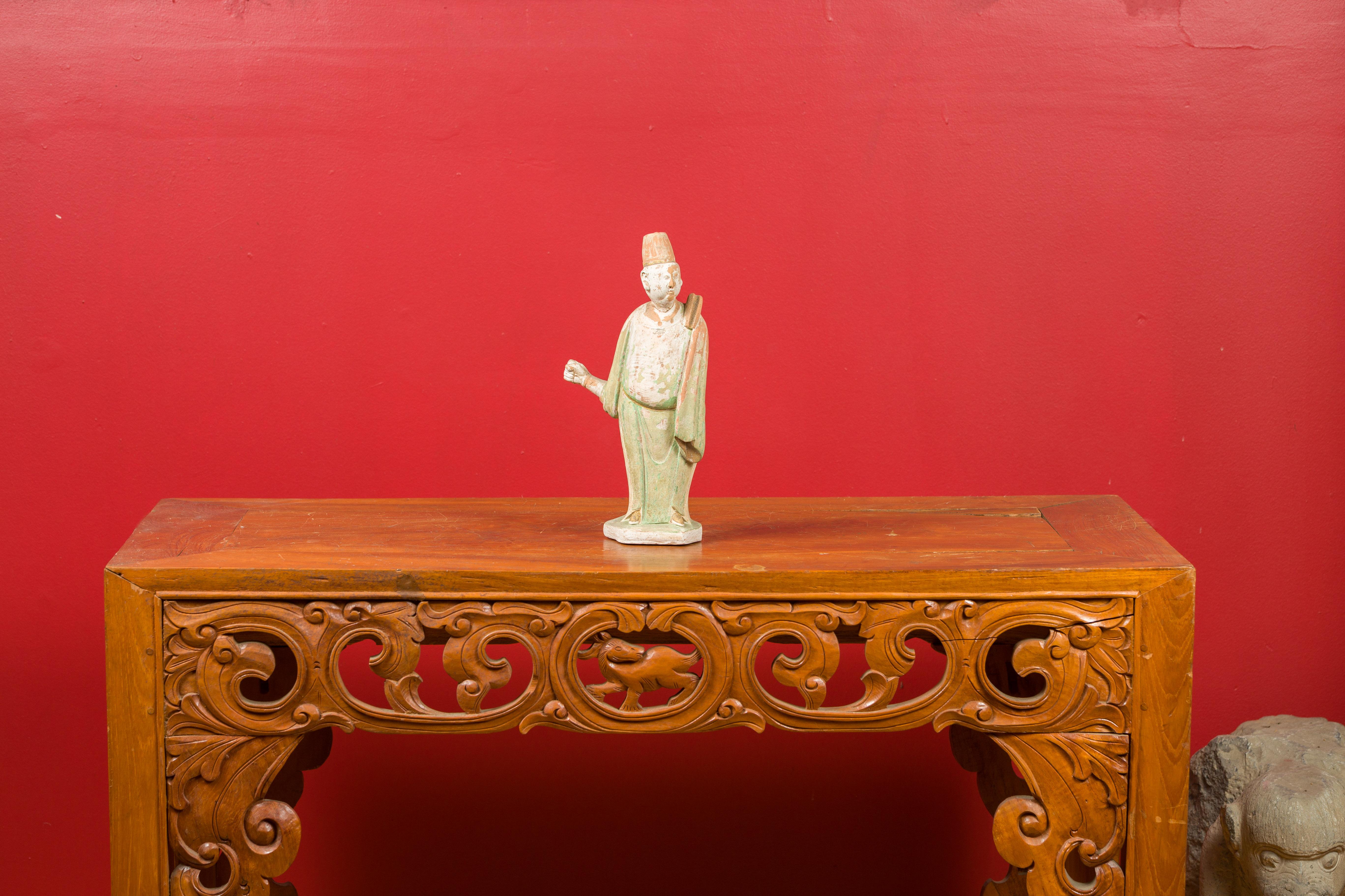 Eine bemalte Terrakotta-Figur aus der chinesischen Ming-Dynastie mit originaler Polychromie. Diese Ming-Statuette, die durch ihr verwittertes Aussehen und ihre subtile Polychromie besticht, zeigt einen Hofmann, der auf einem sechseckigen Sockel