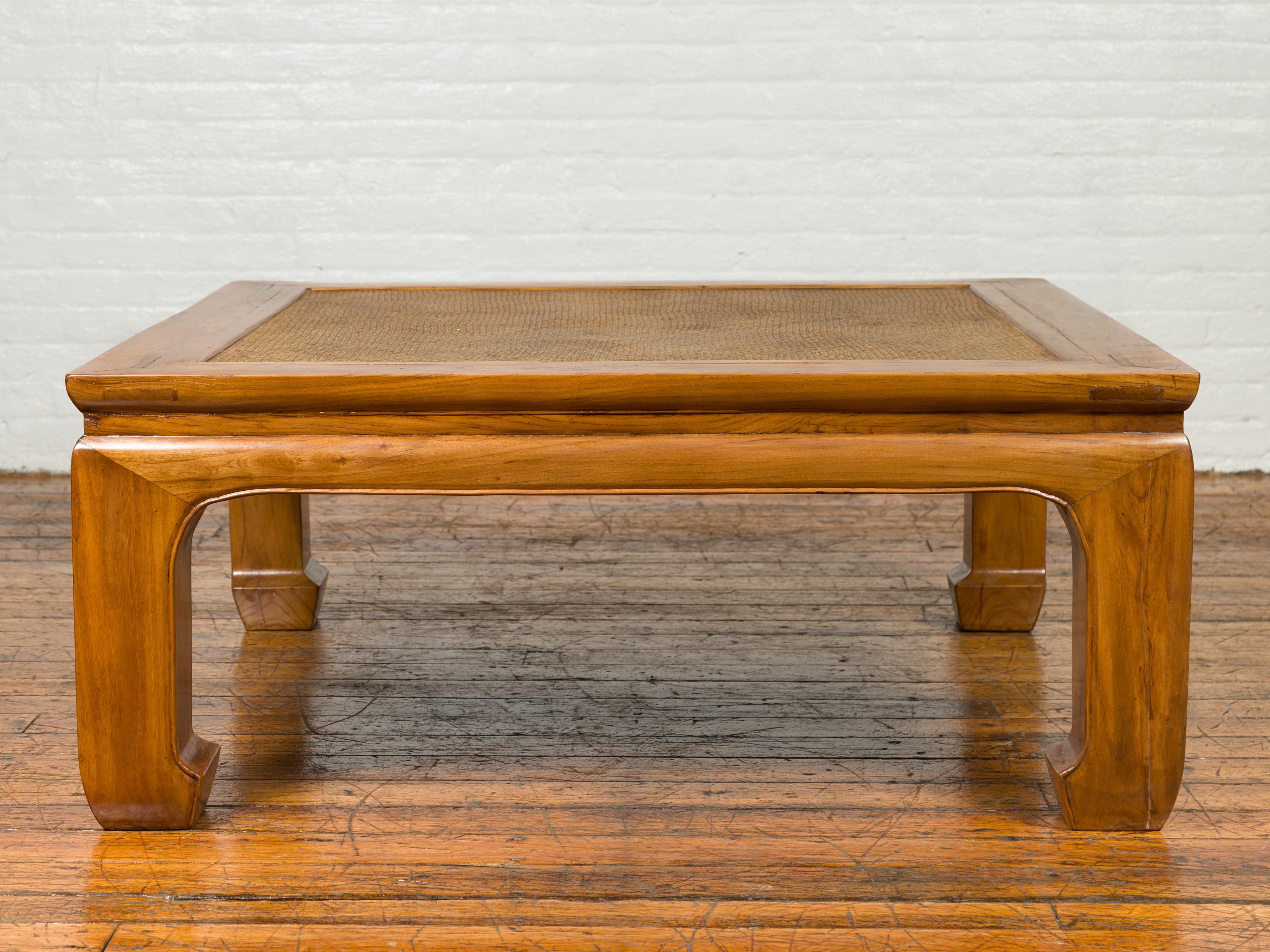 A Chinese Ming Dynasty style elmwood coffee table from the 19th century with rattan inset, waisted apron and chow legs. Born in China during the 19th century, this Ming style coffee table features a rectangular top with rattan inset sitting above a