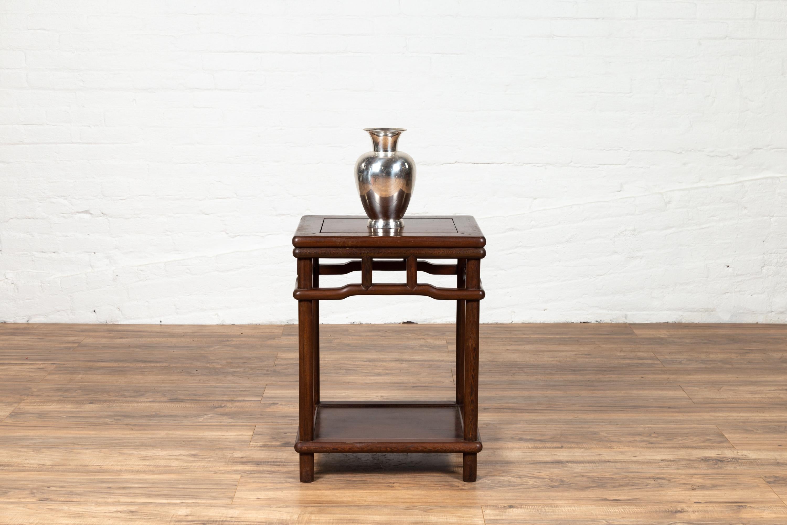 An antique Chinese Ming dynasty style accent side table from the early 20th century with dark wood patina, lower shelf and humpbacked apron. This elegant Chinese side table features a rectangular top with central board, sitting above a humpbacked