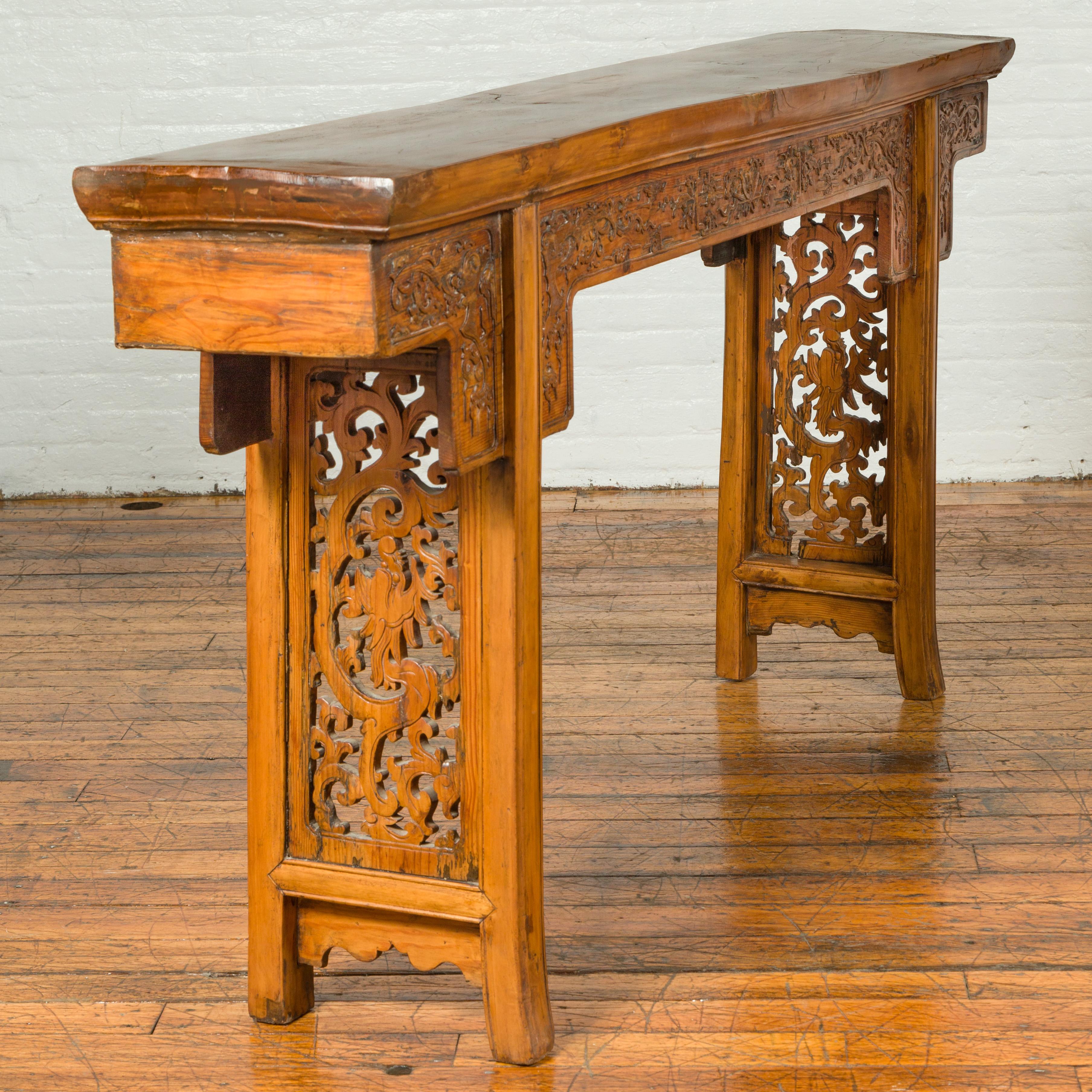 A Chinese Ming Dynasty style altar console table from the 19th century, with scrolls-carved apron, and open fretwork motifs. Attracting our attention with its elegant lines and skilfully carved décor, this Chinese Ming Dynasty style console altar