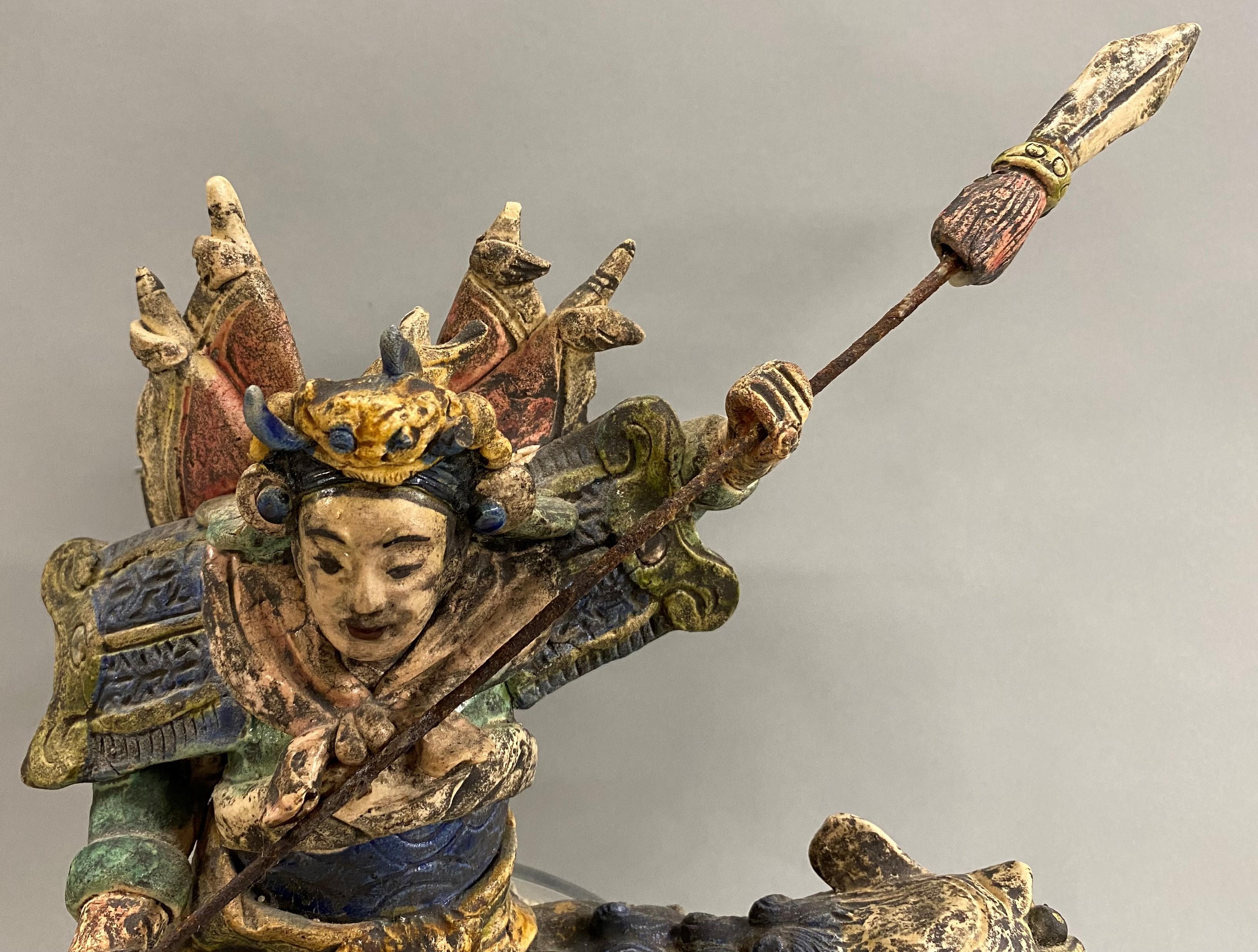Un fragment de tuile en céramique polychrome de style Ming représentant un guerrier sur un dragon avec une lance en métal, joliment monté sur un support en acrylique solide. Datant probablement du 18e/19e siècle, en bon état général, avec quelques