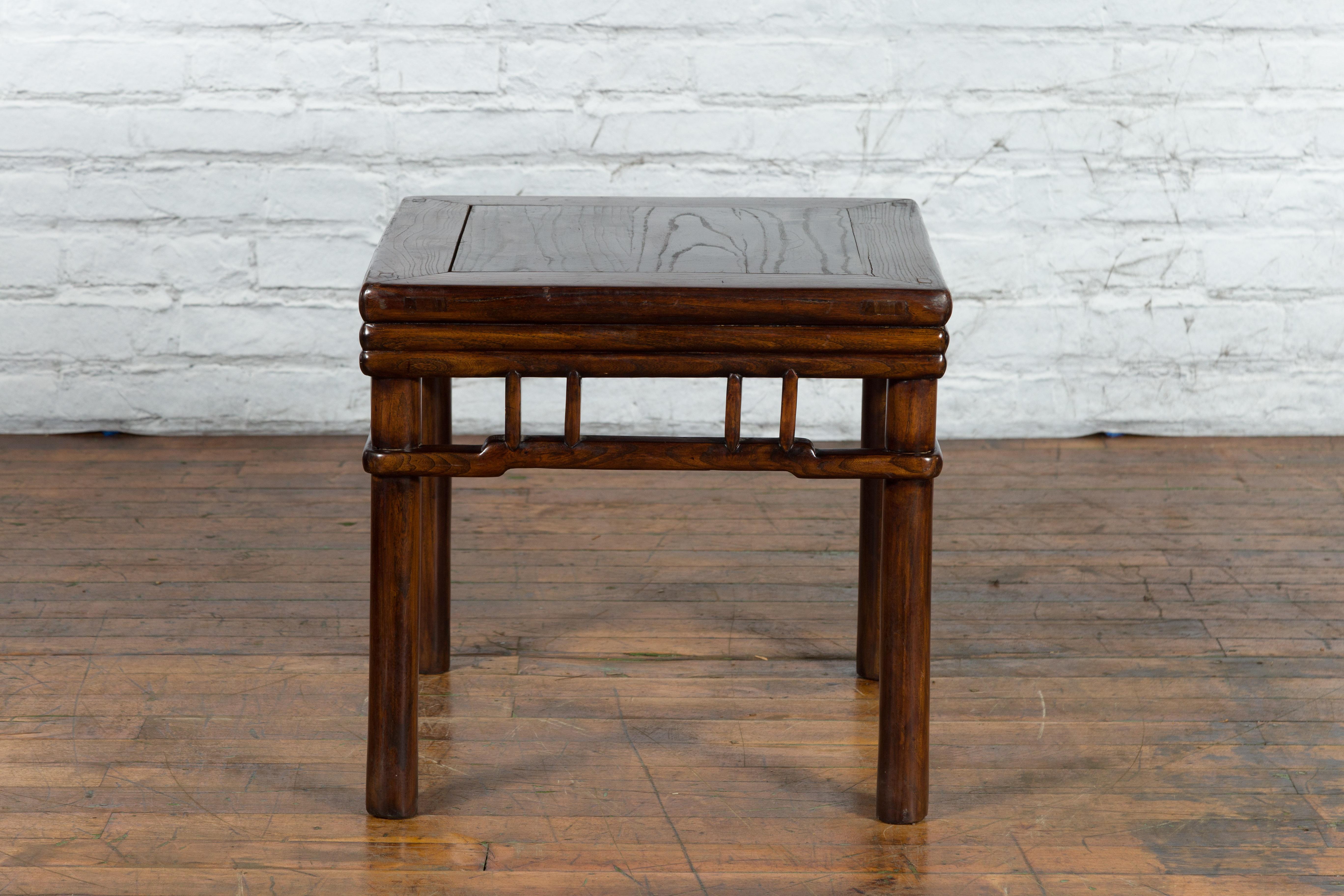 An antique Chinese Ming Dynasty style brown wooden side table from the early 20th century, with reeded apron, pillar strut motifs, hump back stretchers and cylindrical legs. Created in China during the early years of the 20th century, this Ming