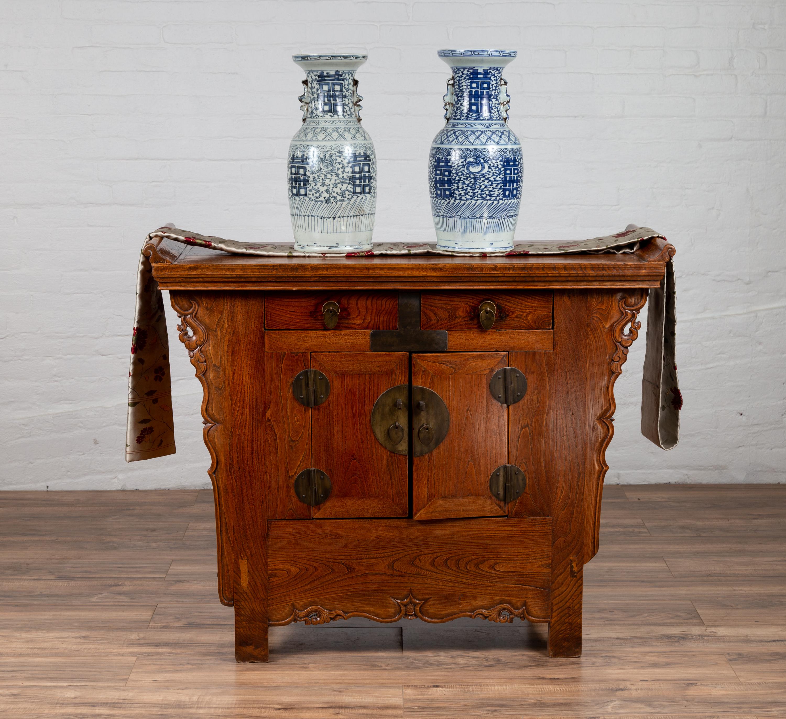 An antique Chinese Ming dynasty style altar cabinet from the 19th century, with everted flanges, two drawers over double doors and carved sides. Behold the resplendent allure of this antique Chinese Ming Dynasty style altar cabinet, a 19th-century