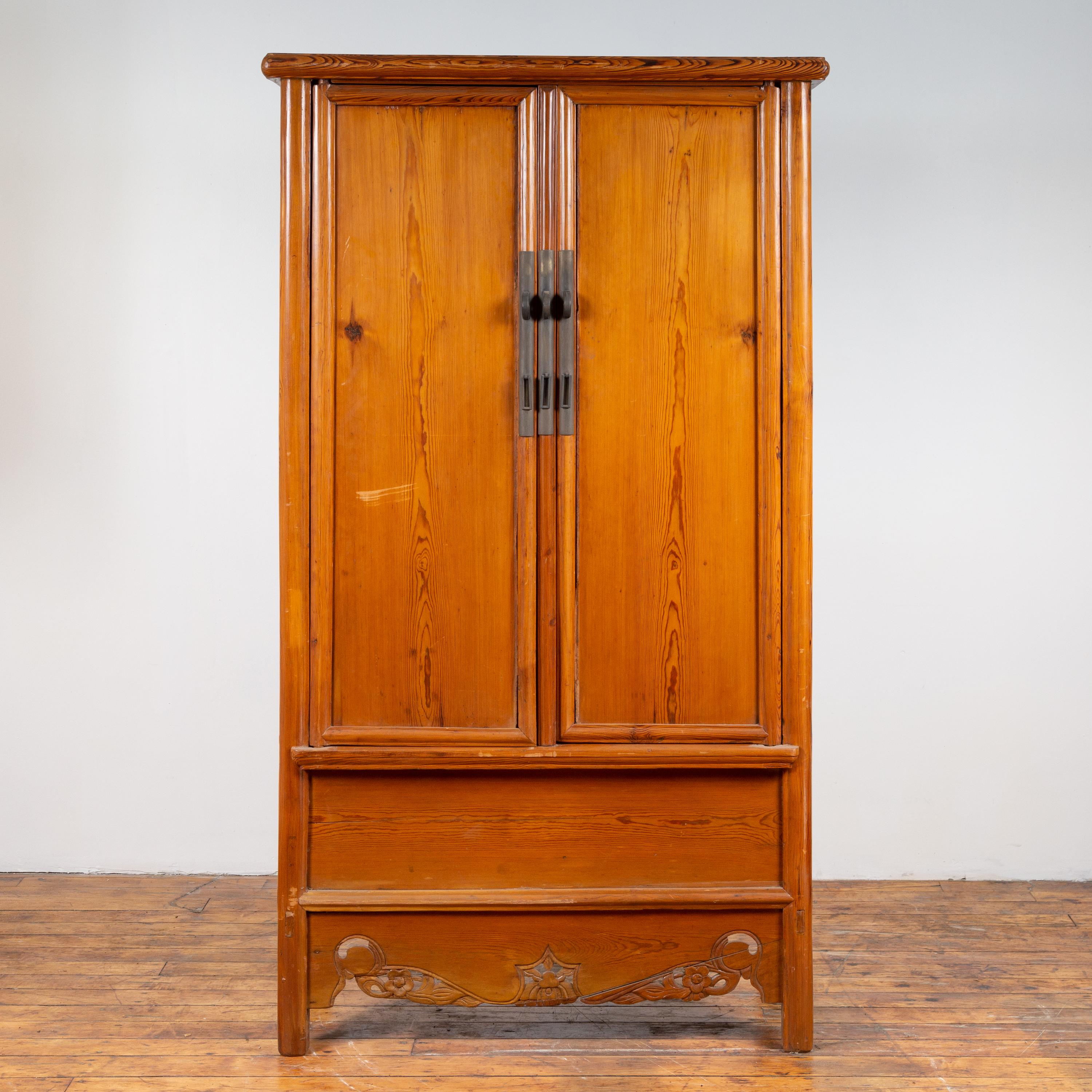 A Chinese Ming dynasty style elmwood wardrobe from the early 20th century, with two doors, hidden drawers and carved skirt. Born in China during the early years of the 20th century, this exquisite elm armoire features a simple cornice overhanging