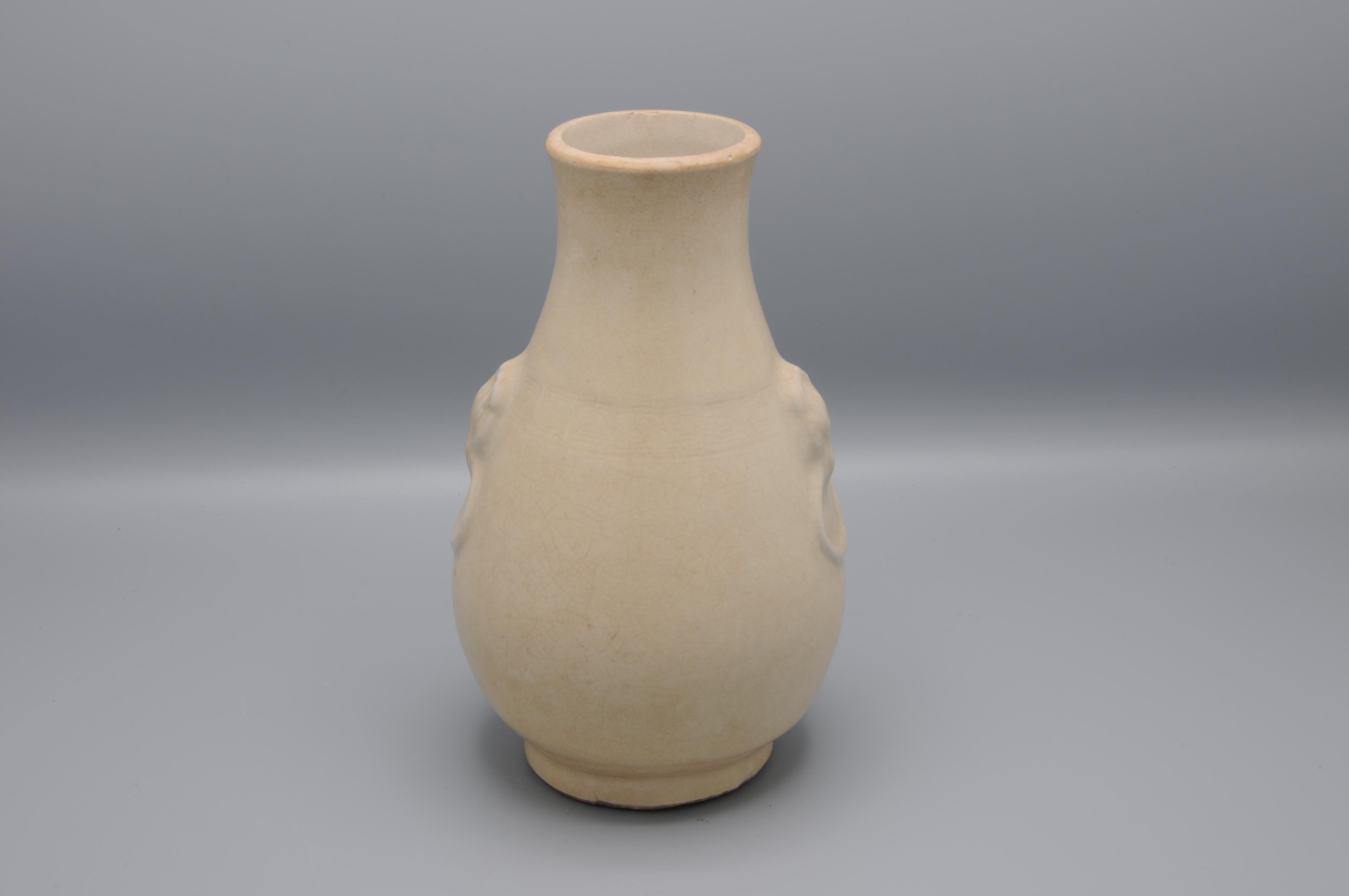 With moulded elephant-head handles, connected by a band of geometric shapes and applied overal with a creamy yellow glaze suffused with a fine crackle.

Condition: the rim polished and a minor glaze-chip to the body.