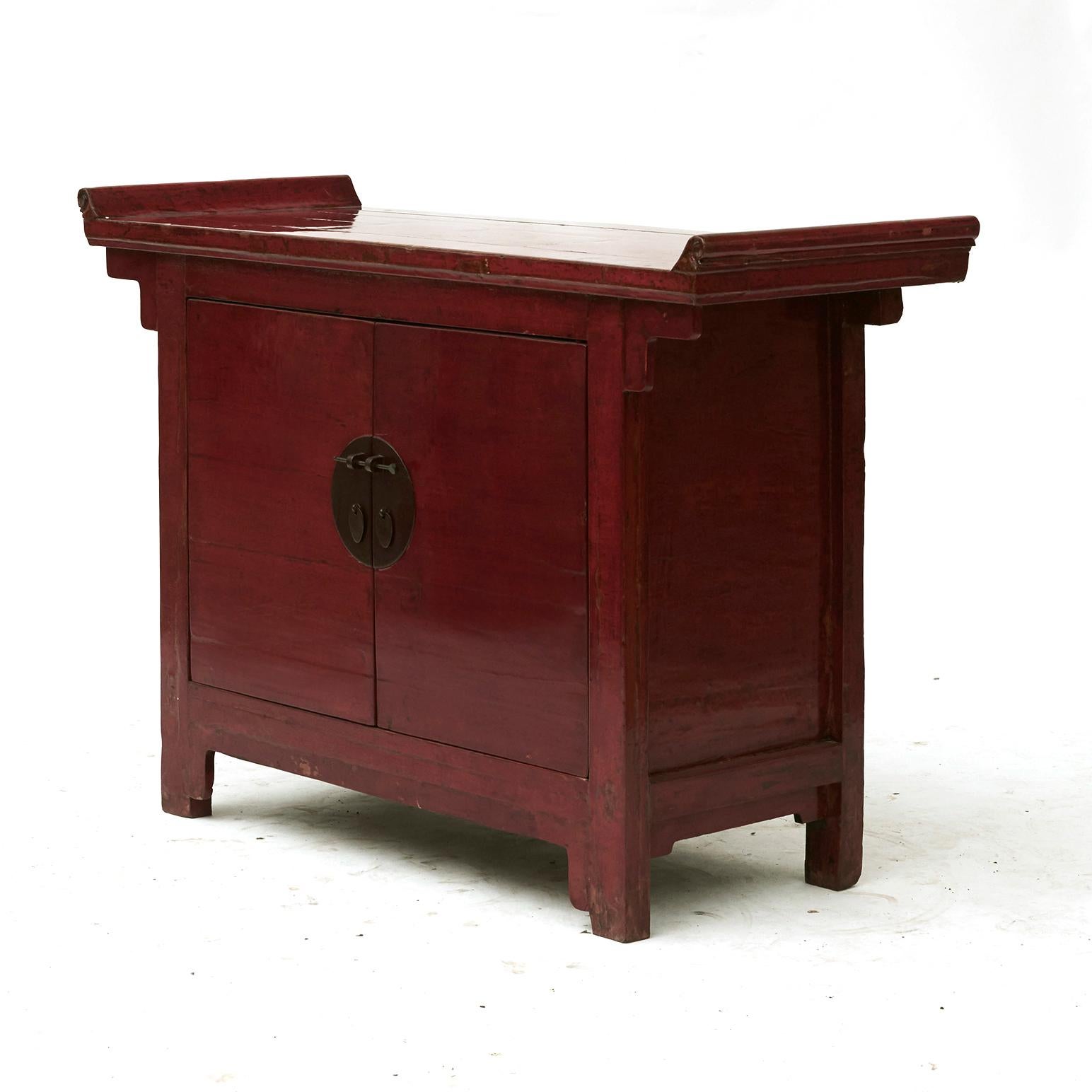 A Chinese Ming Dynasty style altar cabinet with original red lacquer, with natural age-related patina.
The cabinet features a rectangular top with everted flanges, sitting above a façade presenting a pair of double doors fitted with a traditional