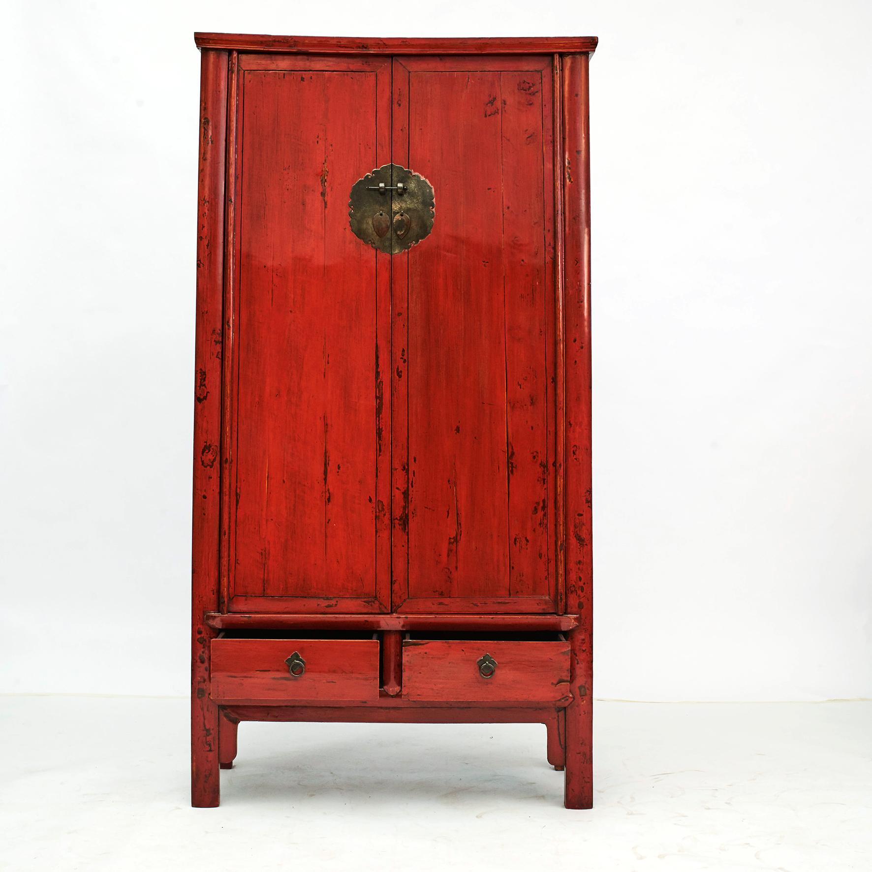 Mid-19th century Chinese wardrobe. Red lacquer with a beautiful age-related patina.
This slightly tapered cabinet features two bottom drawers with ring pull handles.
The doors open via a traditional Chinese lockset sitting on a central medallion.