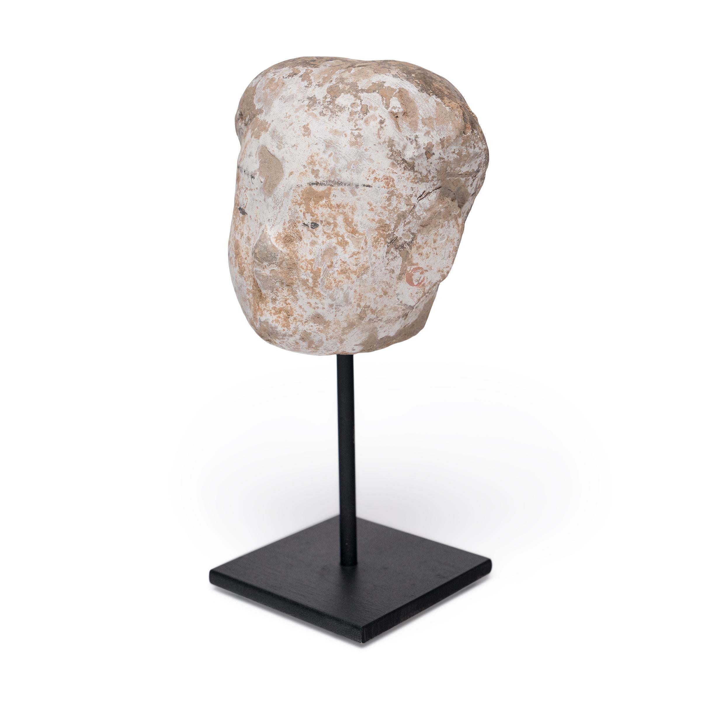 Questo piccolo busto in ceramica è la testa di un attendente personale della dinastia Han (206 a.C. - 220 d.C.). Un tipo di statuetta funeraria nota come míngqì, l'attendente sarebbe stato incluso nelle offerte funerarie per salutare e accompagnare