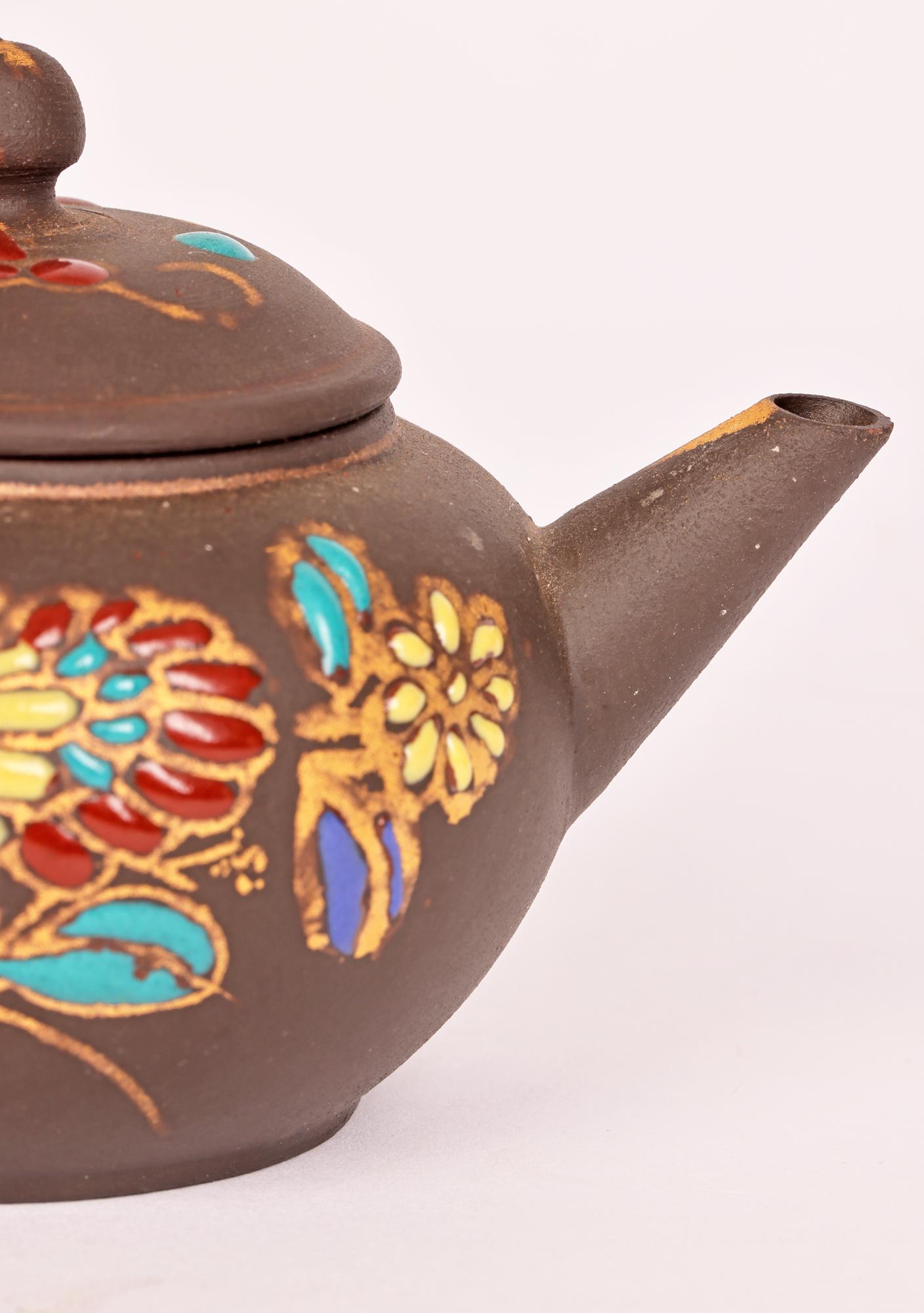 A fine vintage Chinese miniature teapot hand applied with enamel floral designs dating from the mid 20th century. The lightly potted teapot is of squat rounded shape with a loop handle and short pouring spout and with a slightly domed fitted cover.