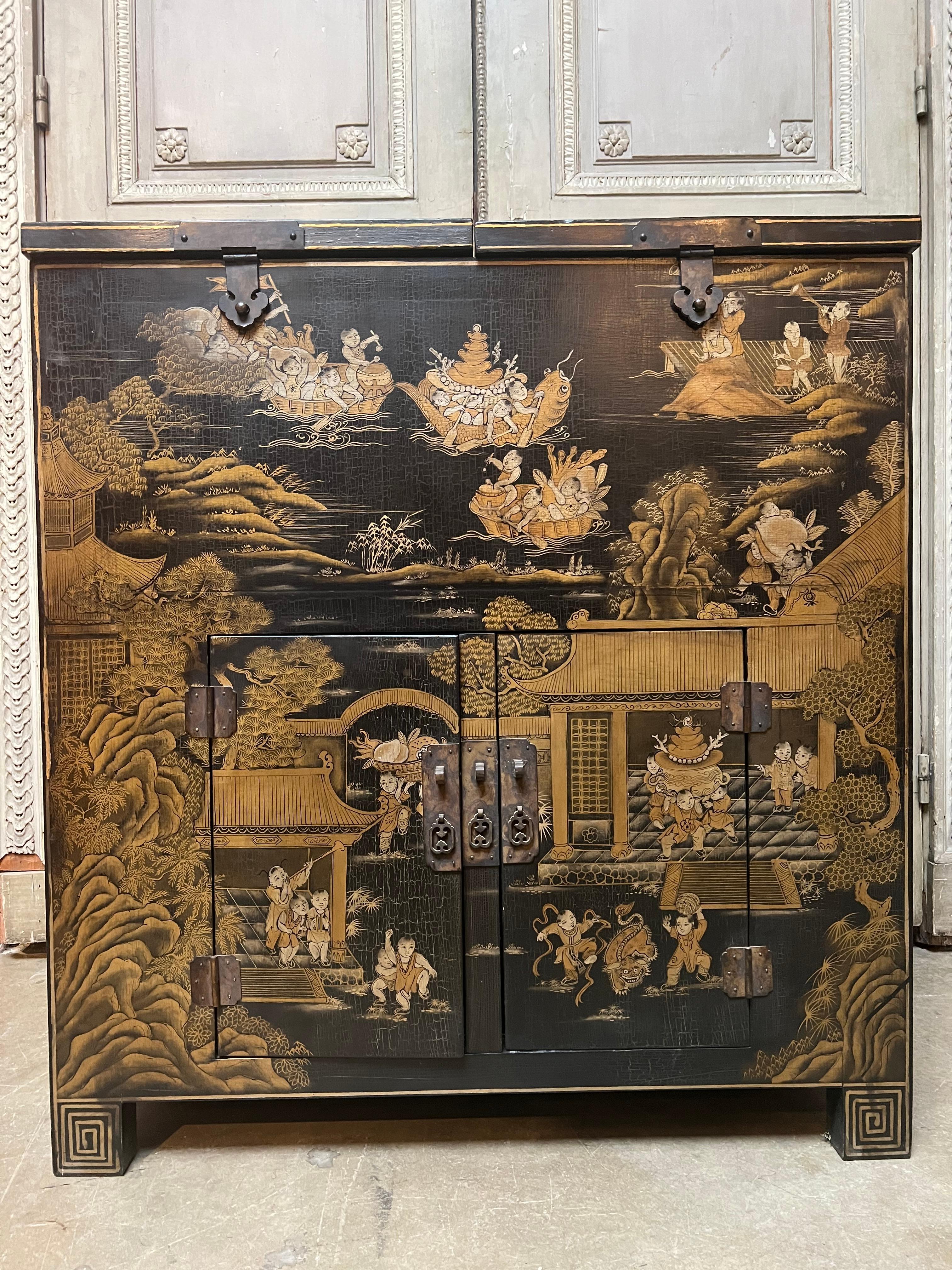 A Chinese black lacqured chest with gilt decoration was originally used to hold gold coins. This highly decorative cabinet is beautiflly decorated with multible children in various scenes This piece is an older reproduction made in the Canton region