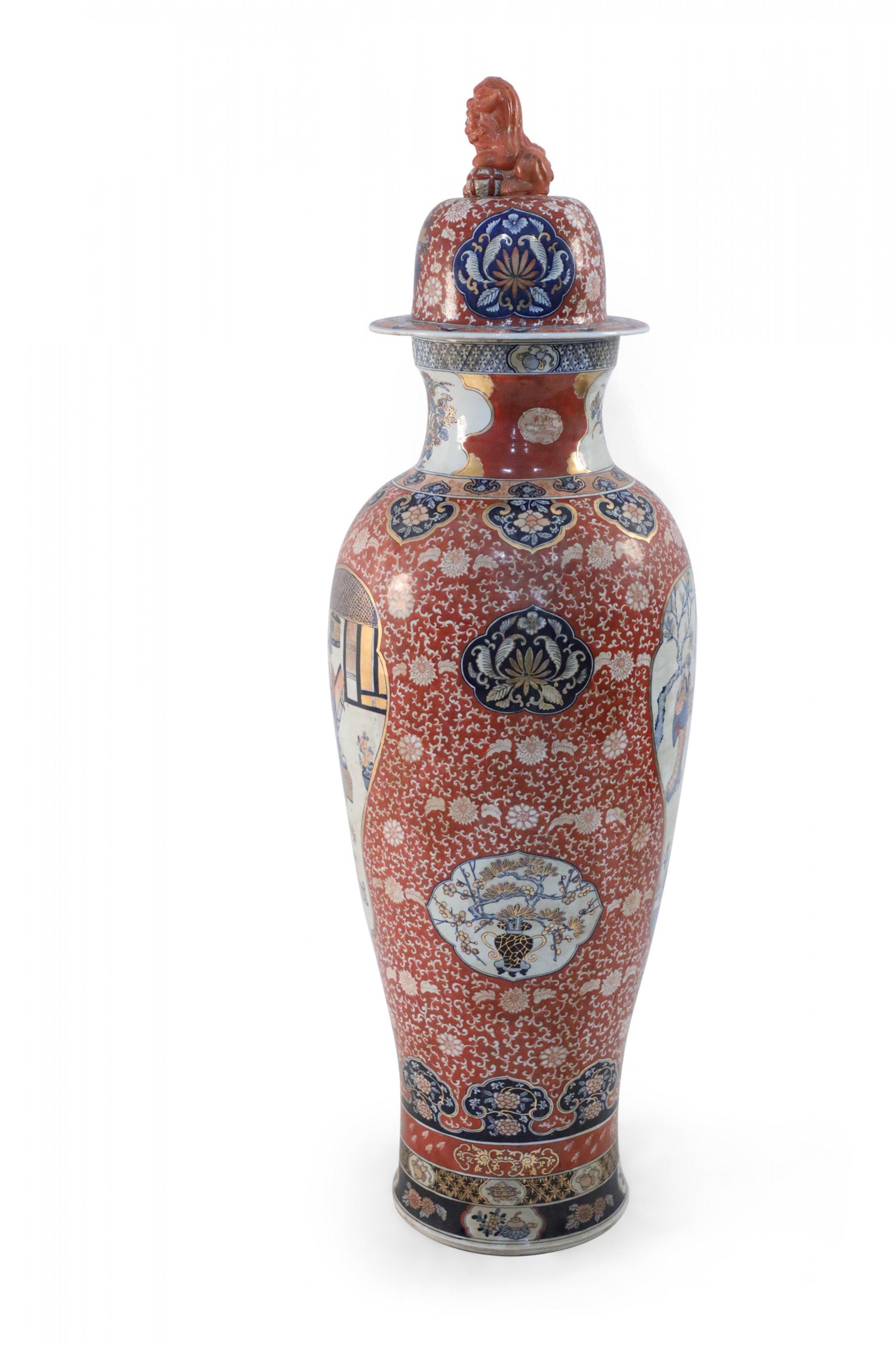 Chinese monumental lidded urn celebrating Japanese Imari ware in both palette and design, featuring medallions with figurative scenes against an orange, floral patterned ground and topped with a foo dog-finial lid.