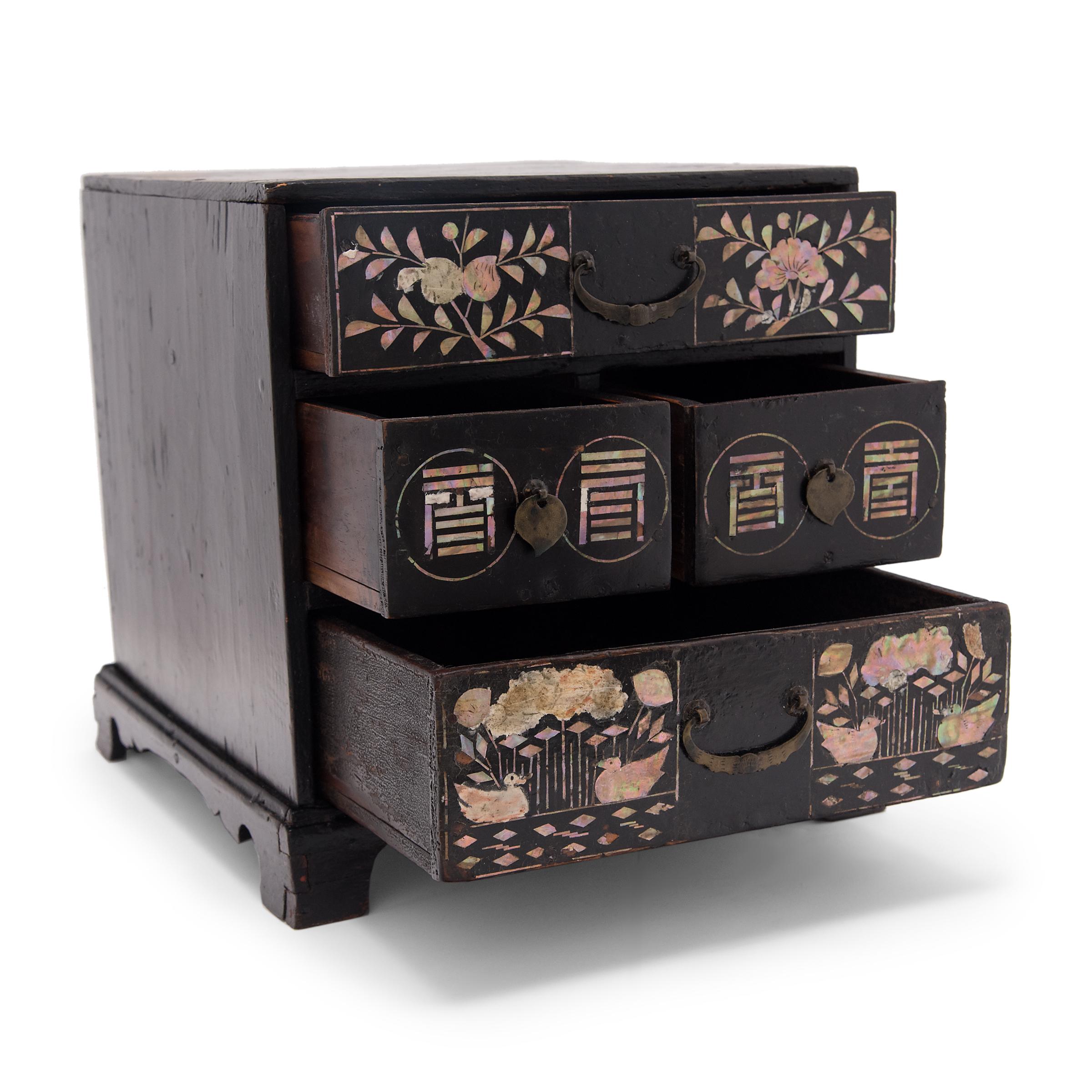 Dated to the early 20th century, this four-drawer table chest was likely used a jewelry box and is beautifully decorated with black lacquer inlaid with mother-of-pearl. The top drawer is patterned with elegant floral branches and the bottom drawer