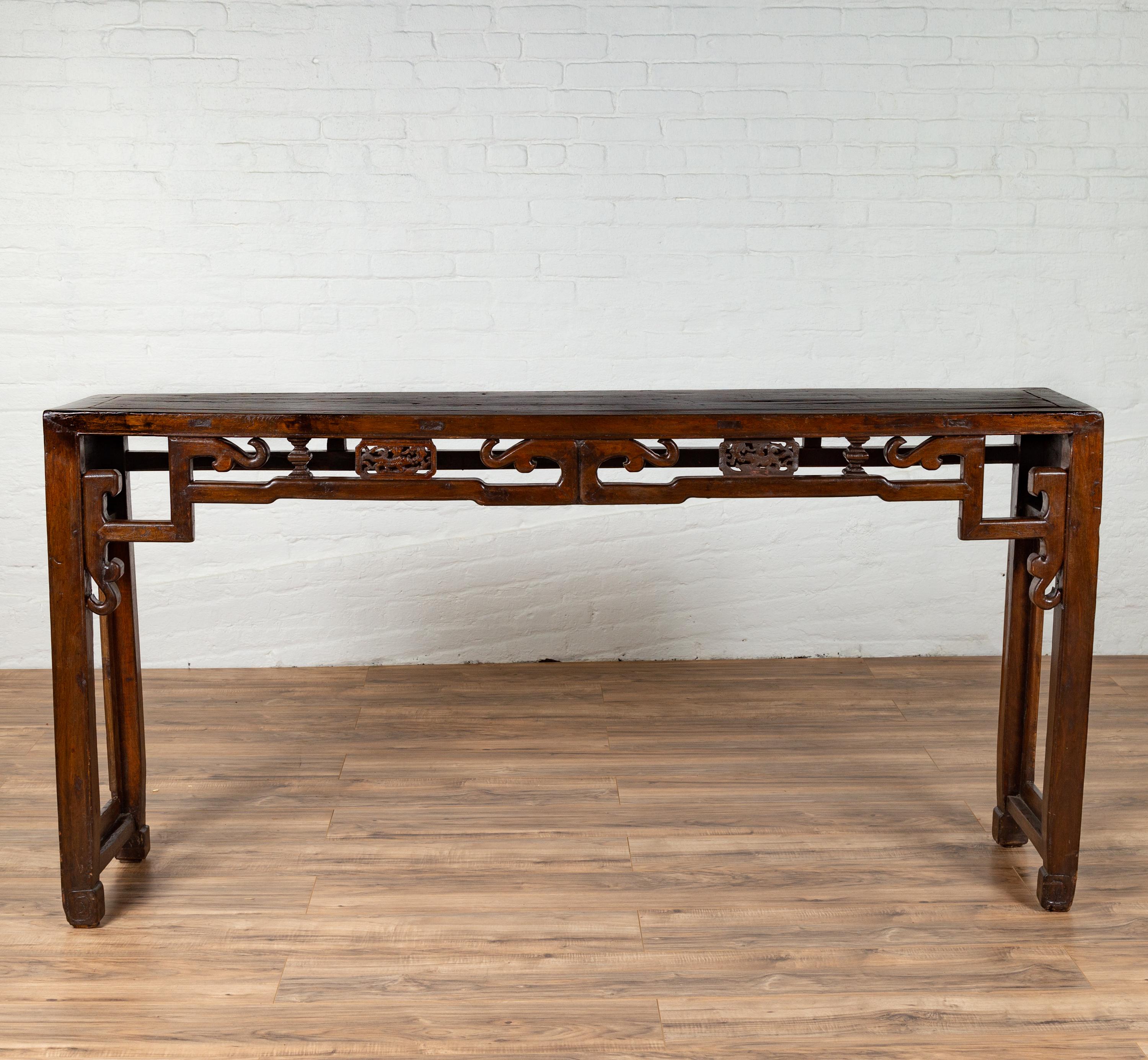 A Chinese narrow altar console table from the 19th century, with open fretwork frieze, horse hoof legs and unusual raised panels. Born in China during the 19th century, this exquisite wooden altar console table features a narrow rectangular top with