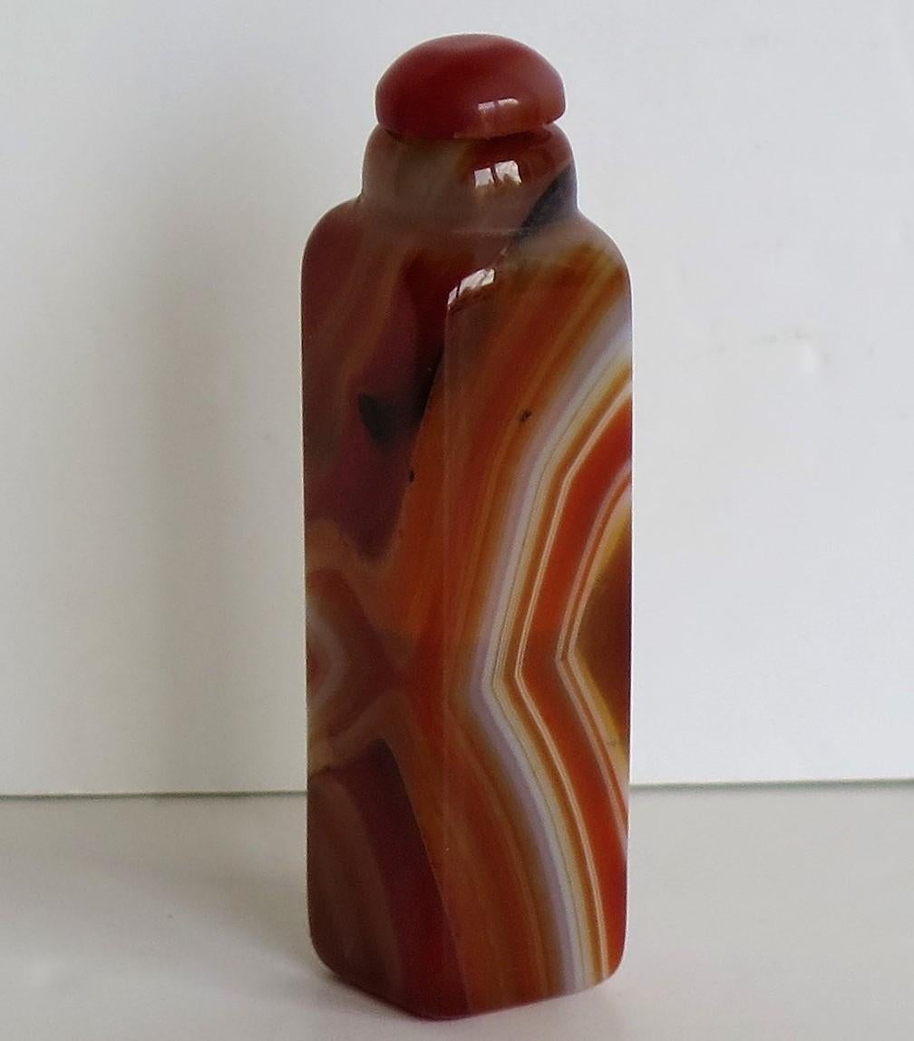 This is a beautiful Chinese Export snuff bottle, complete with its top and made from natural agate stone, having lovely veined colors, which we date to the earlier part of the 20th century.

The bottle has a square carved section with a short neck