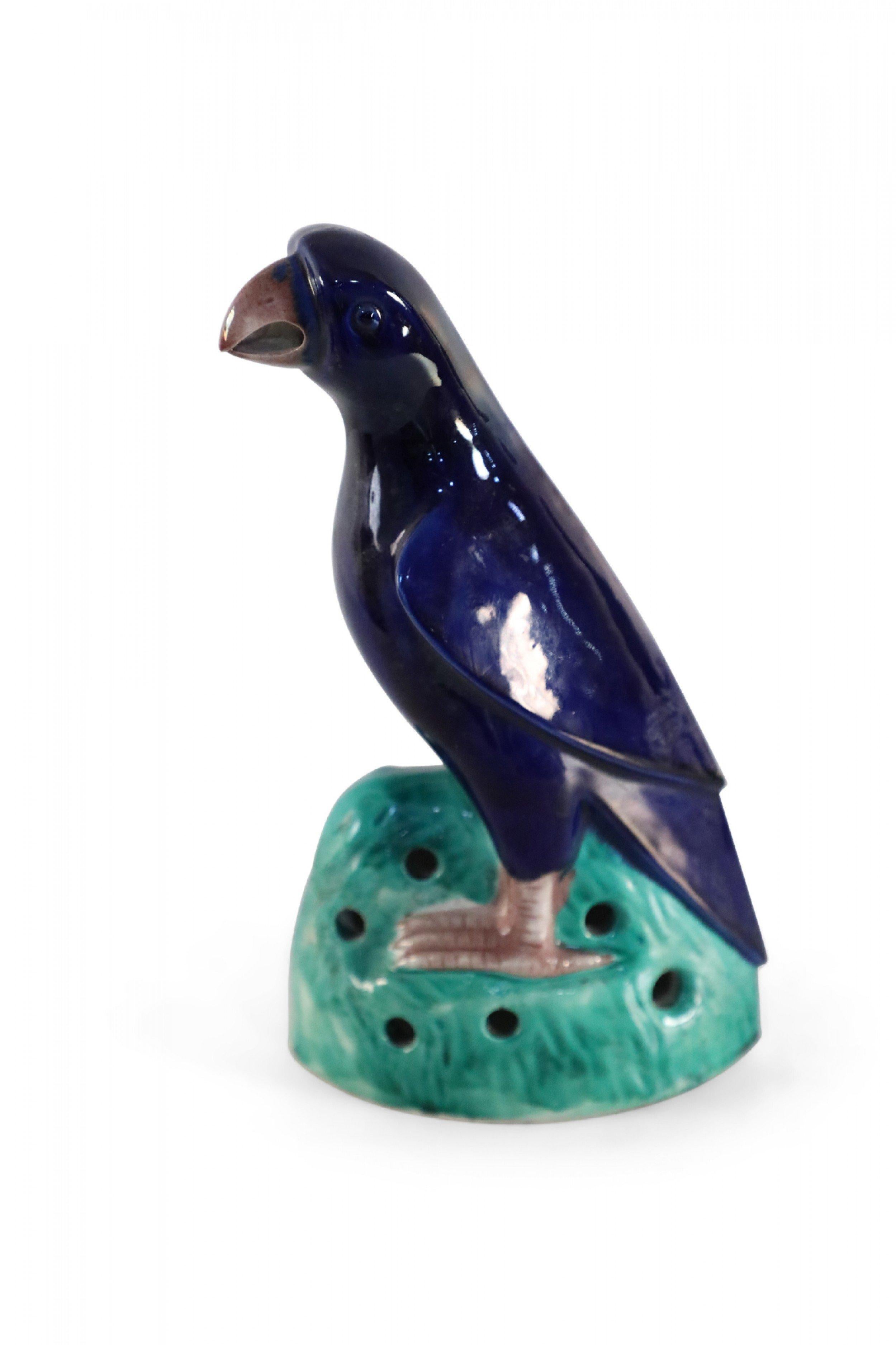 Vintage Chinese glazed porcelain statue of a navy blue parrot with a brown beak and talons perched atop green grasses. 
      
