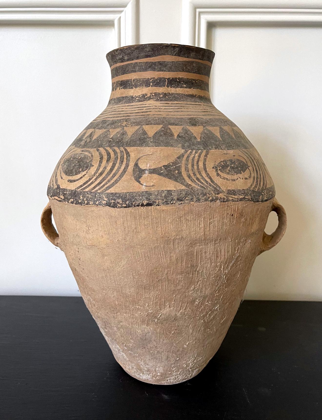 This large Chinese neolithic jar was likely from one of the cultural clusters along the Yellow River in Northern China such as Yangshao culture (5000-3000BC). The coarse earthen ware features a bulbous body, a short neck opening to a round mouth and