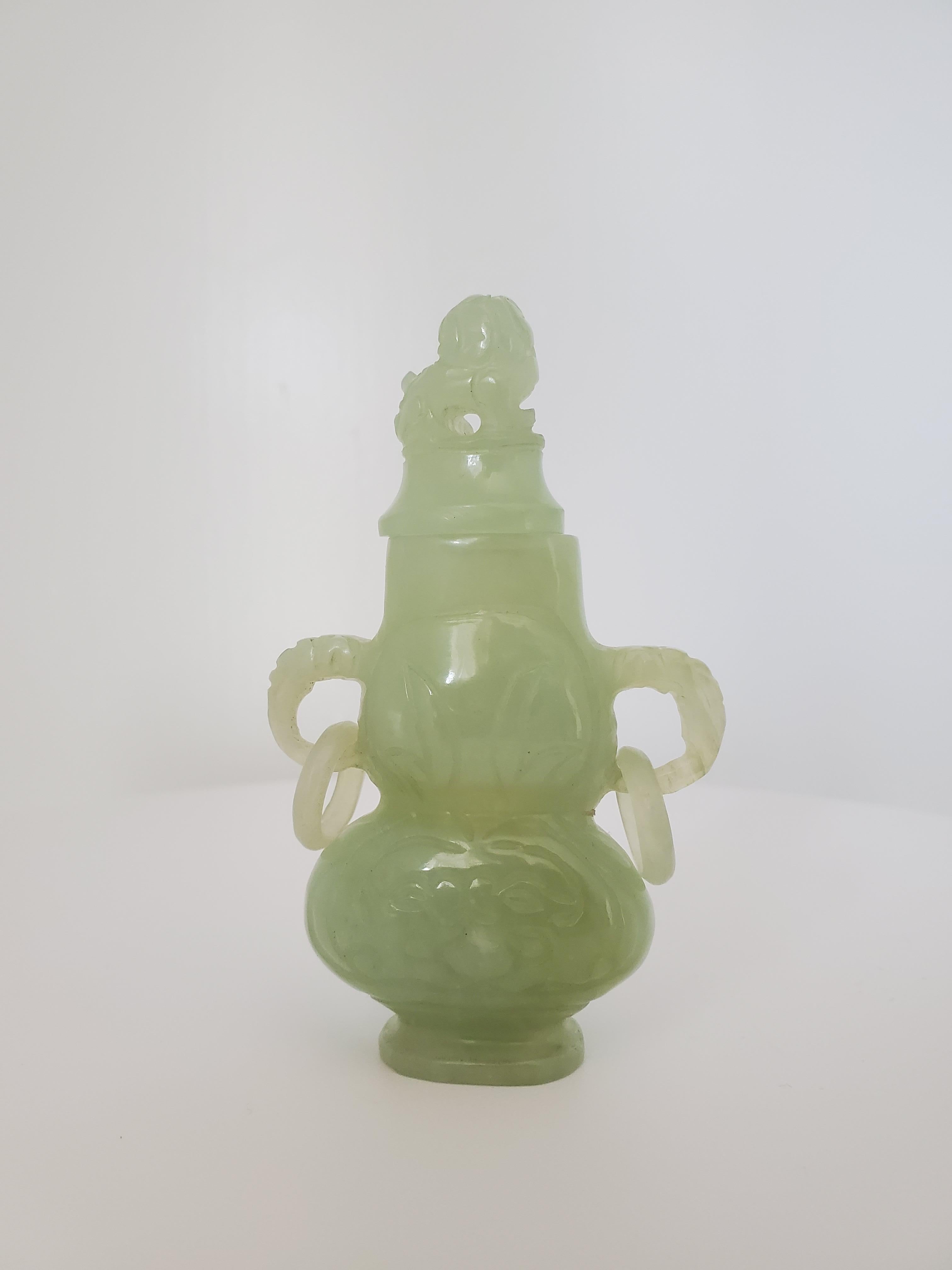 This archaistic style lidded vase or censer is a lovely piece of jade. It consists of a flattened baluster body and figural handles with hanging rings. The front and back body are carved with archaistic masks and the lid is a carved figural of a
